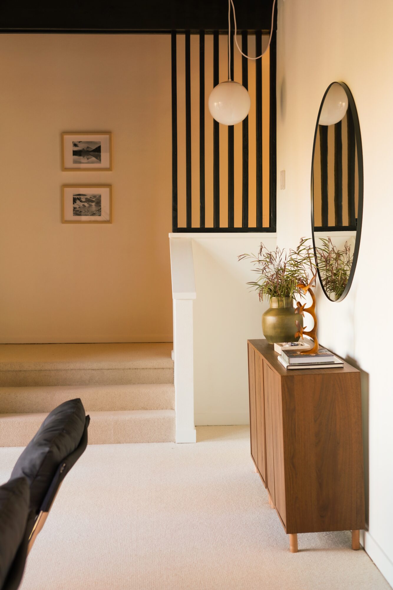 Interior entryway with a wooden sideboard, vase with flowers, oval mirror, and staircase with framed pictures on the wall.