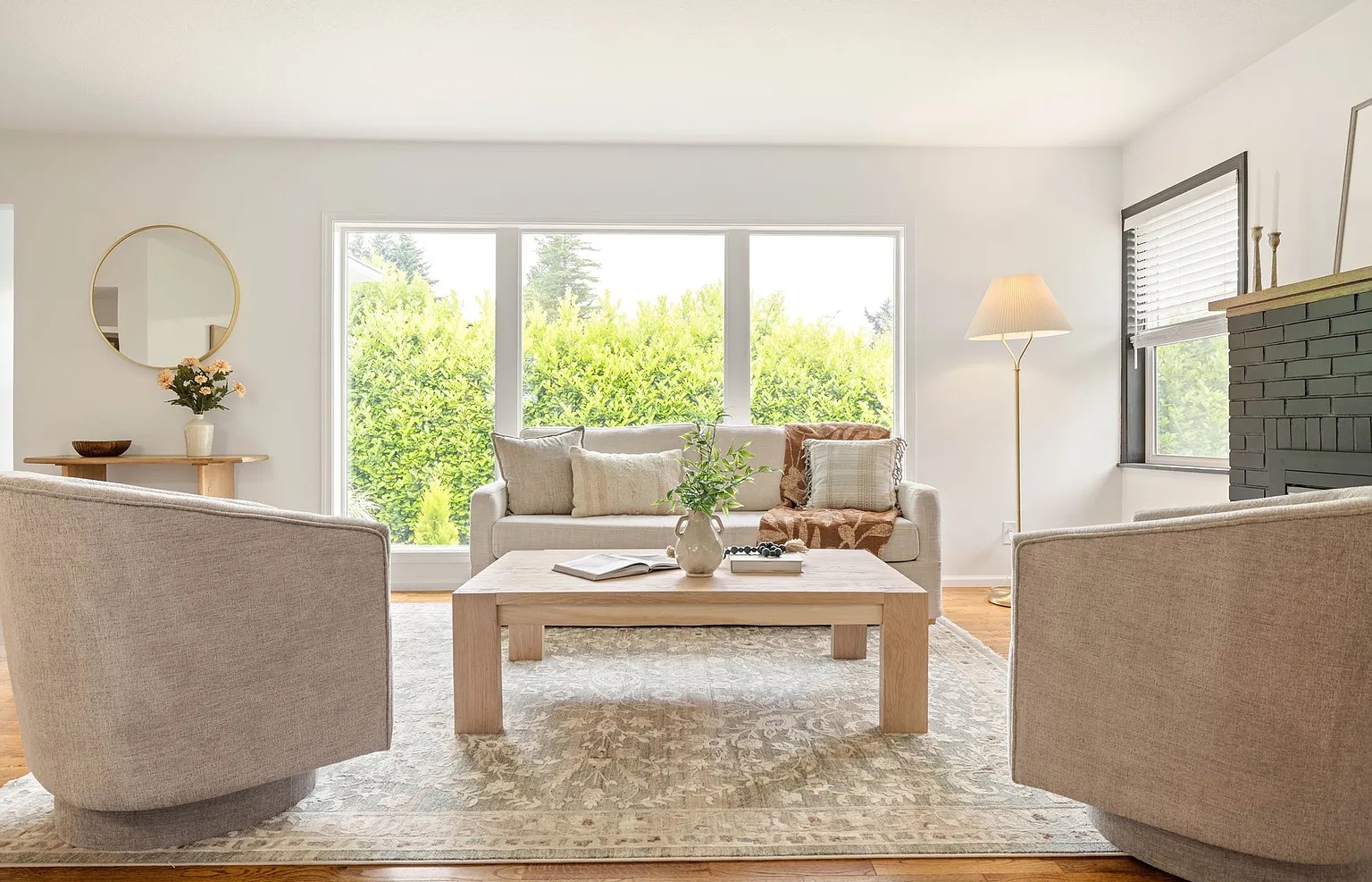 Living room with large window, two armchairs, a sofa, a coffee table, and a floor lamp, bright and airy.