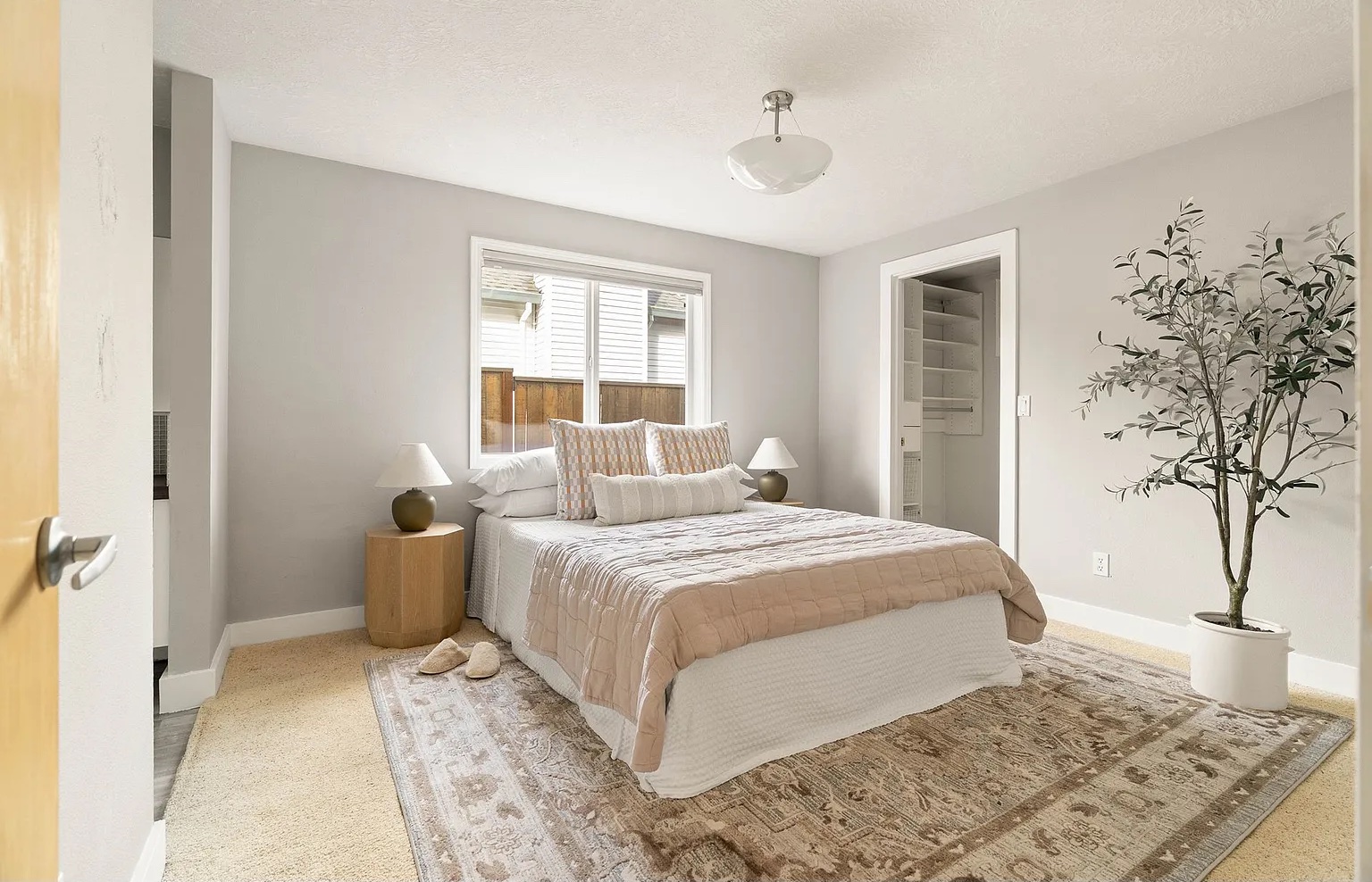 Bedroom with bed, two nightstands, window, potted plant, and beige rug, bright and airy with white walls.