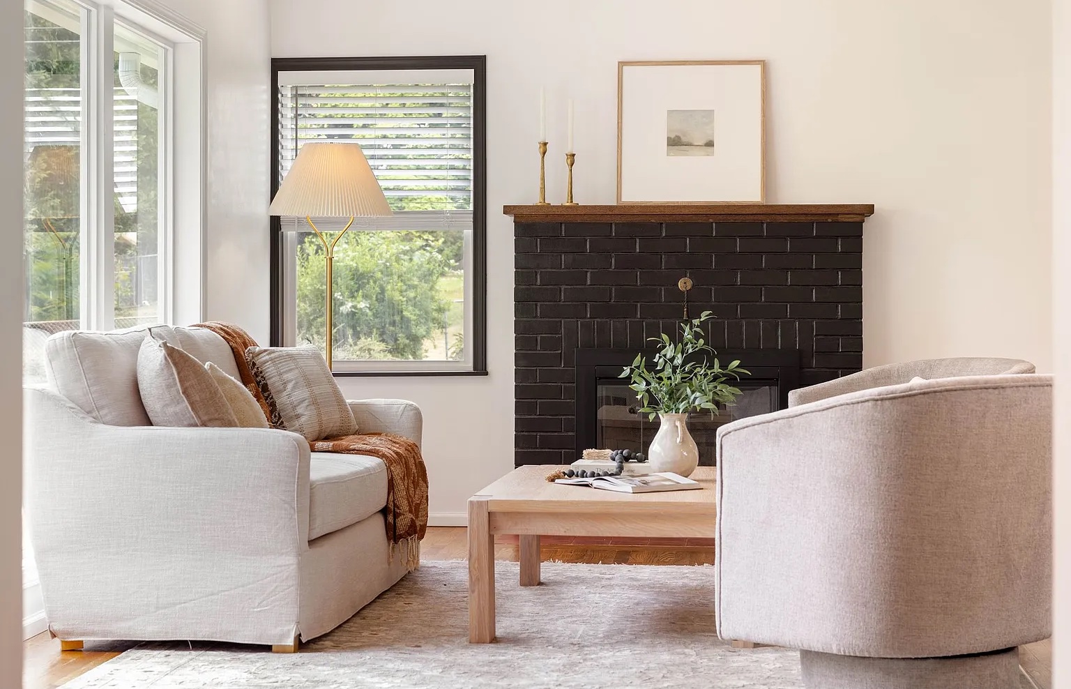 Living room with a white sofa, a wooden coffee table, a black brick fireplace, and a window with a view outside.