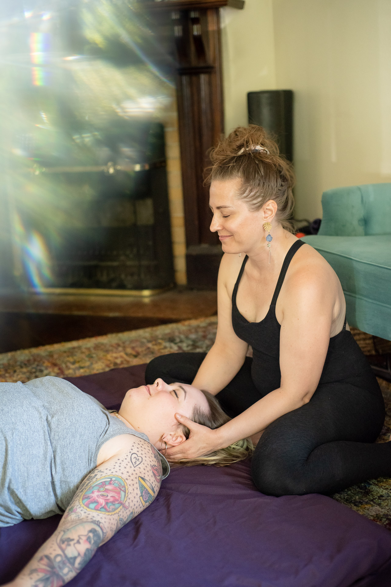 Woman practicing yoga with a person lying on the floor, holding their face, in a living room setting.