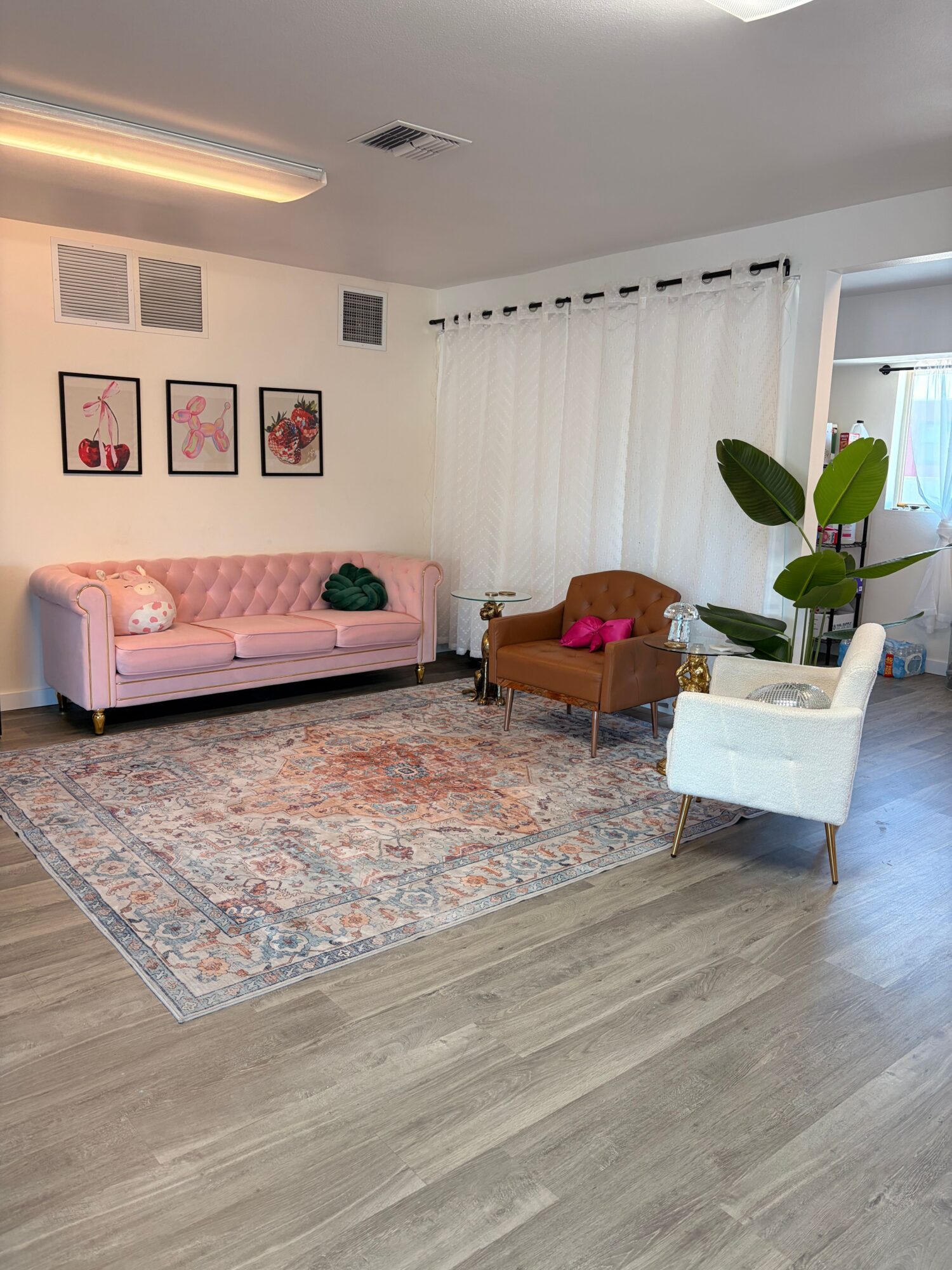 Living room with pink sofa, white side table, potted plant, and framed artwork on wall.