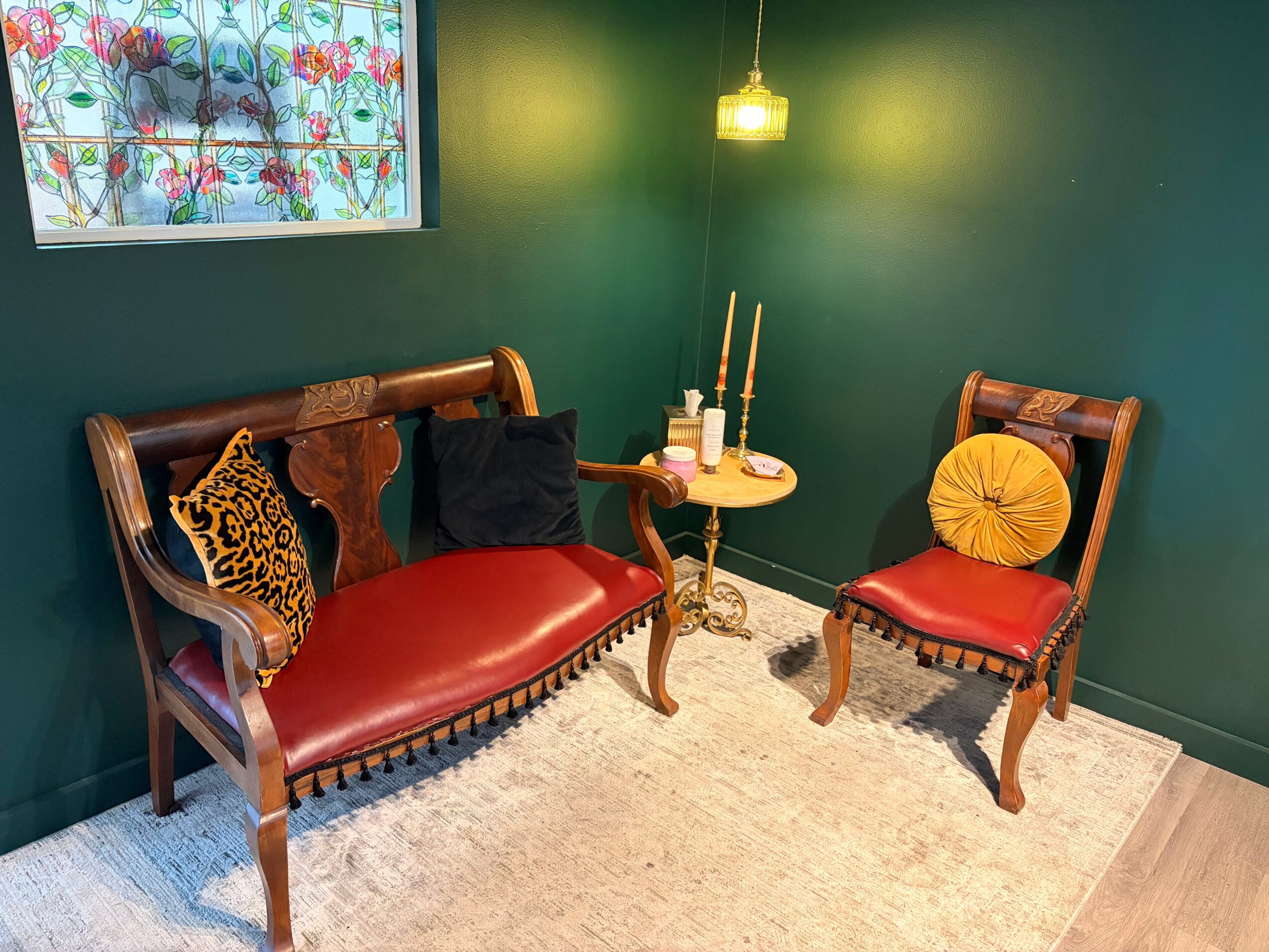 Living room with green walls, wooden furniture with red cushions, a small round table, and a window with floral curtains.