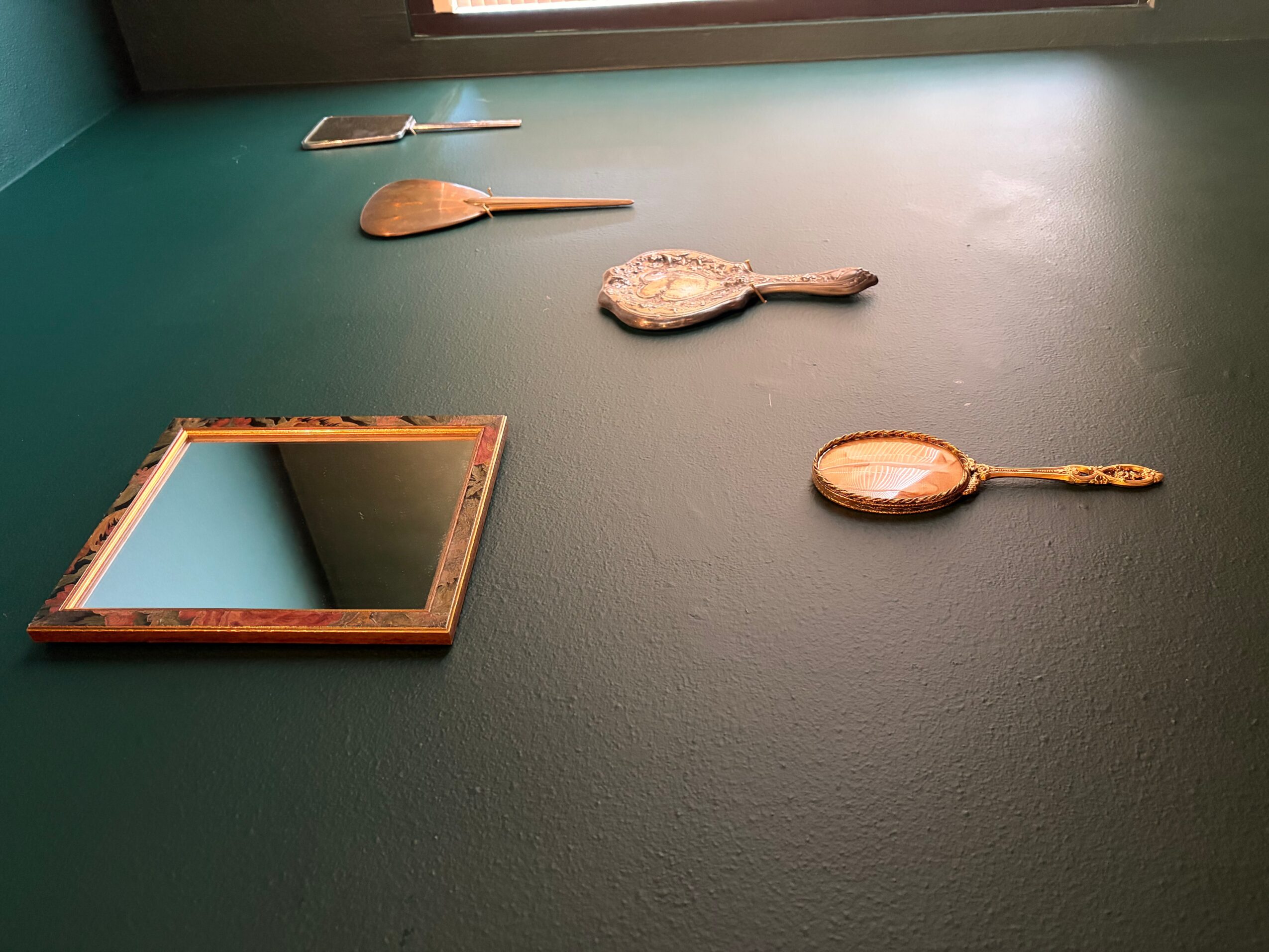 Four wooden spoons and a mirror on a green surface, with a window above. The image is rotated 90 degrees clockwise.