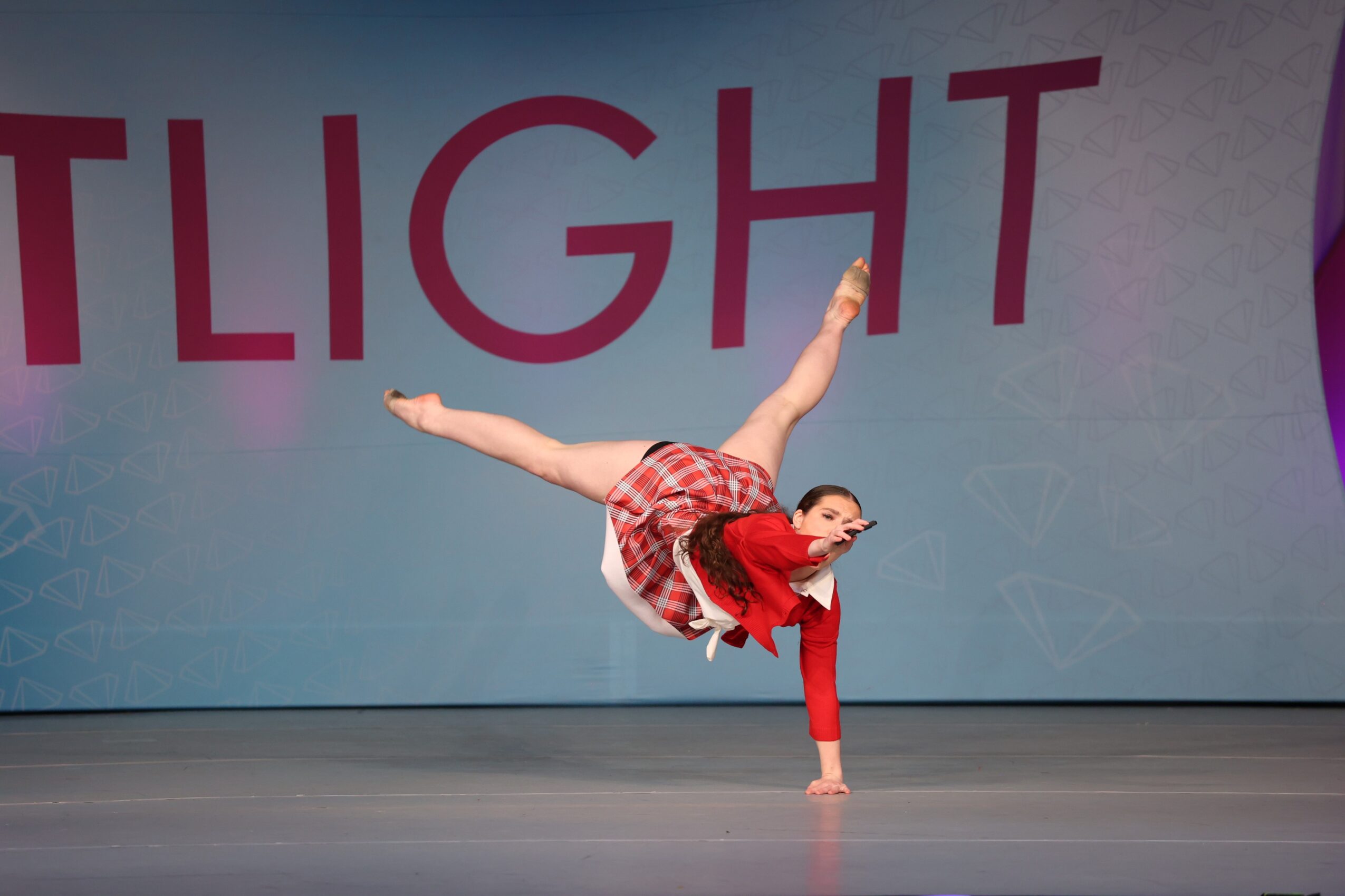 A young girl performs a handstand on stage with a large backdrop reading 'SPOTLIGHT'.