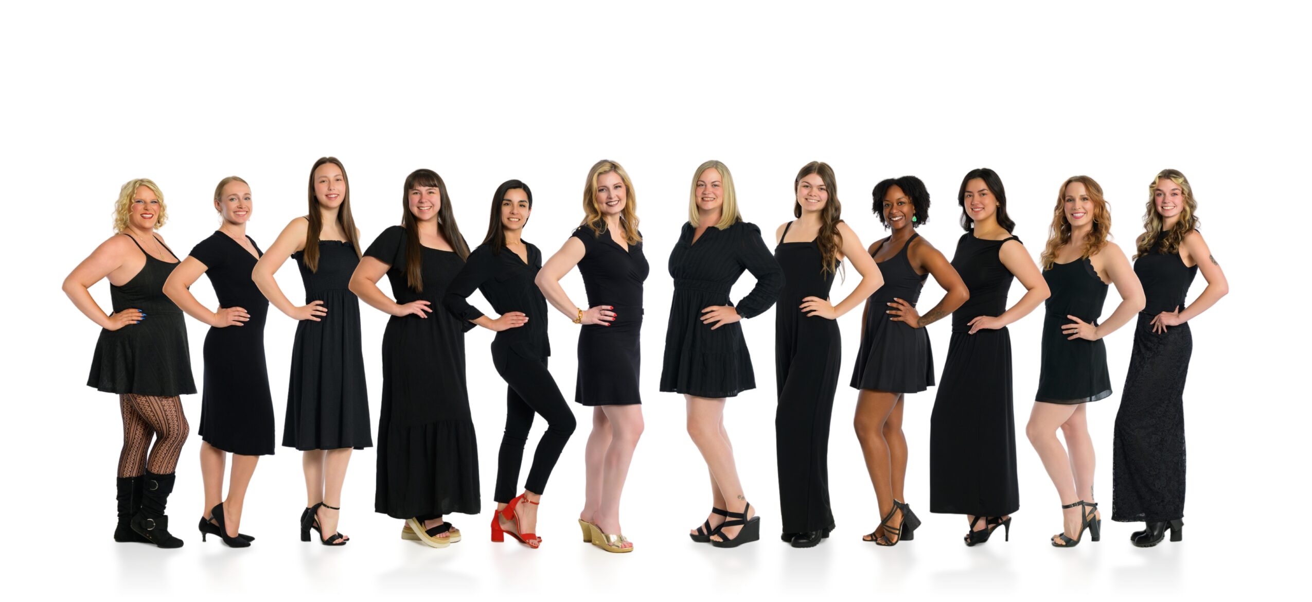 Group of women standing in a line, hands on hips, wearing black dresses and heels, smiling.