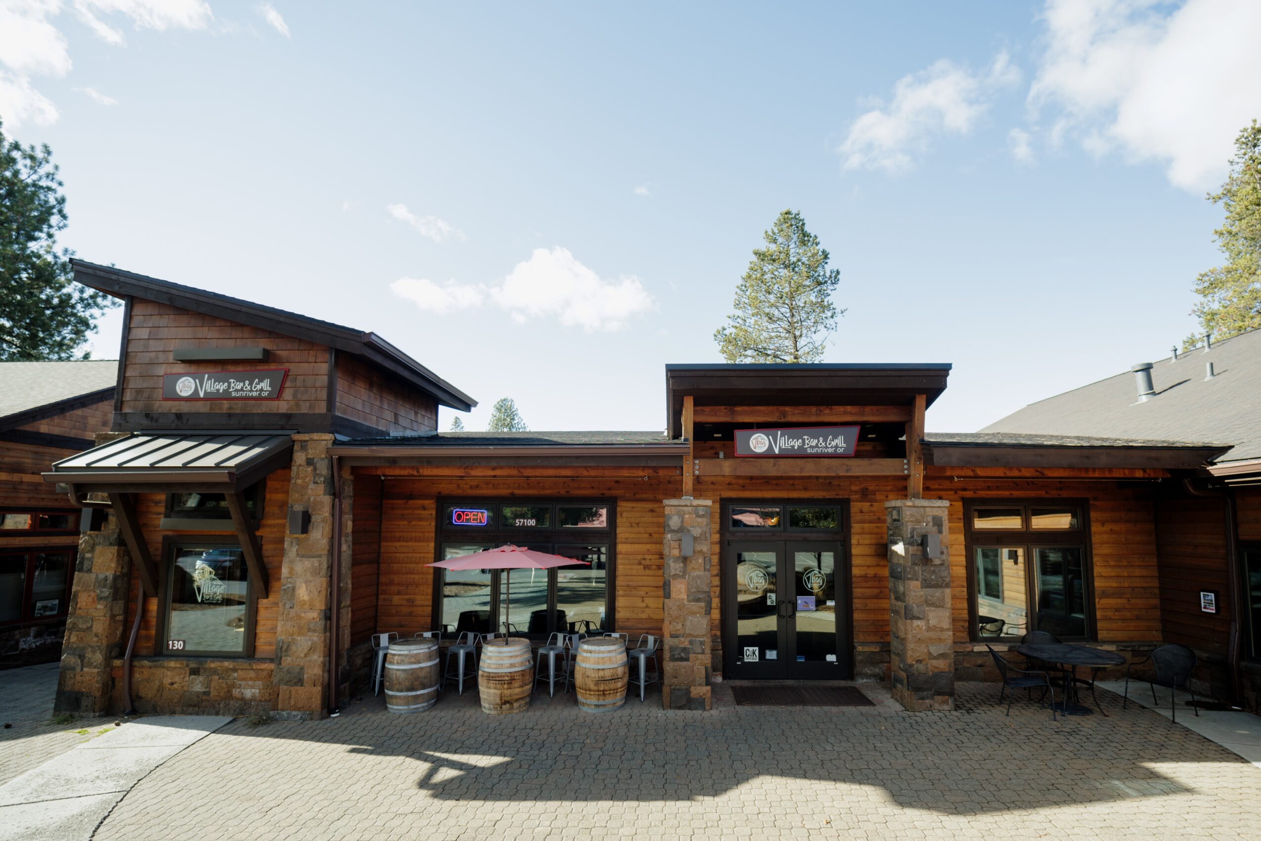 Front view of a wooden building with glass doors and barrels outside, under a partly cloudy sky.