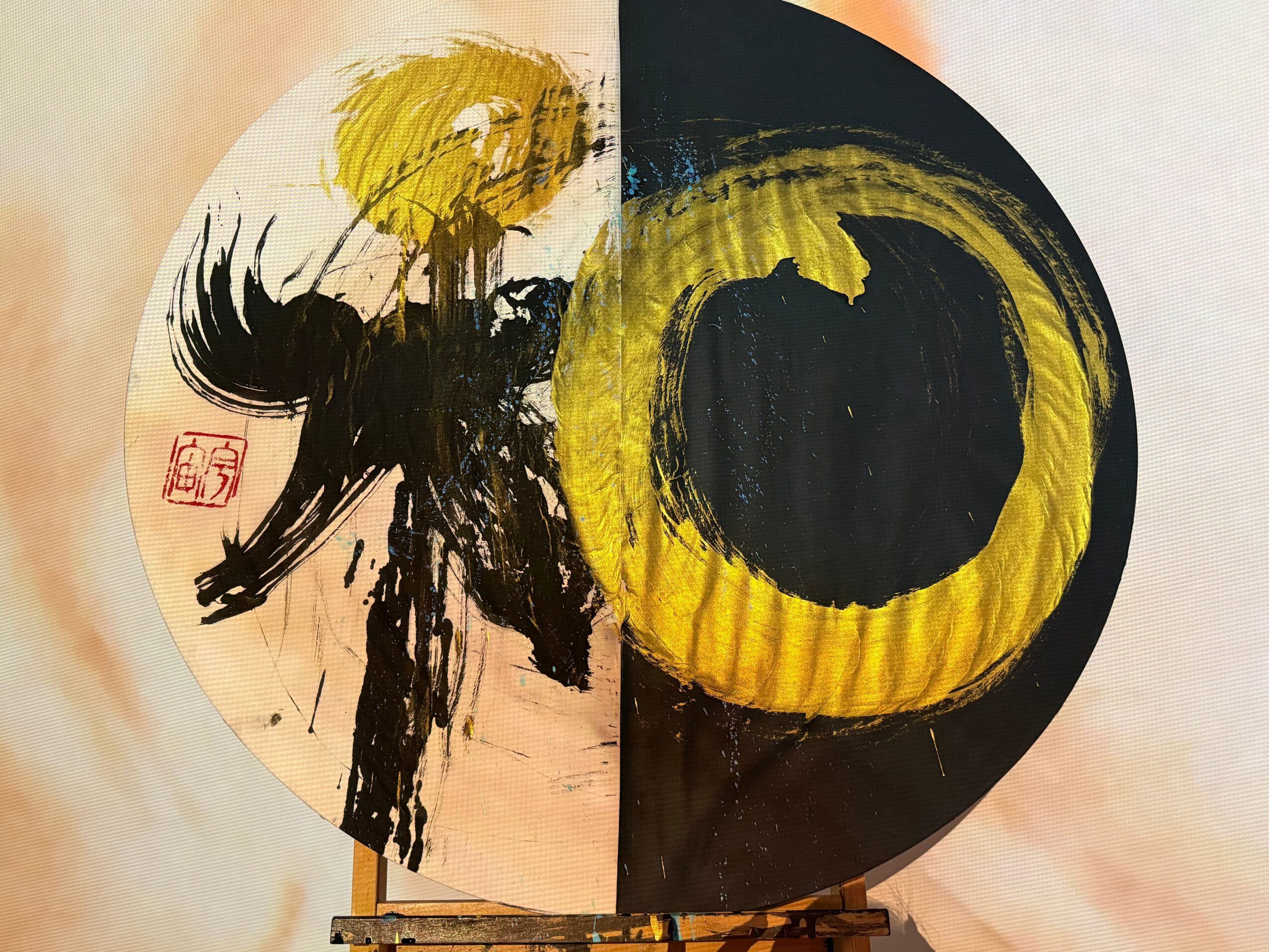Circular artwork with black, yellow, and white paint, featuring abstract brushstrokes and a red stamp, divided into two halves.