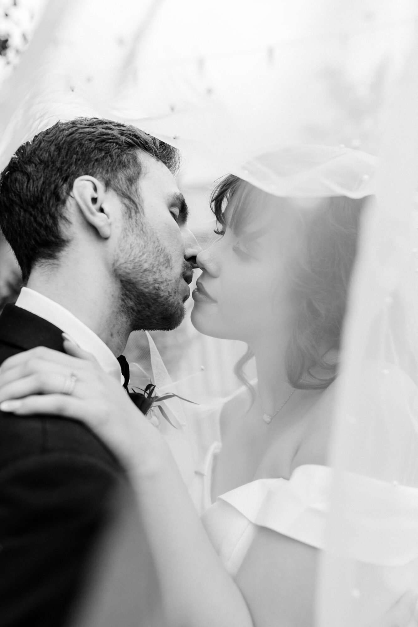 A couple about to kiss, with the man on the left and woman on the right, both in wedding attire, close-up shot.