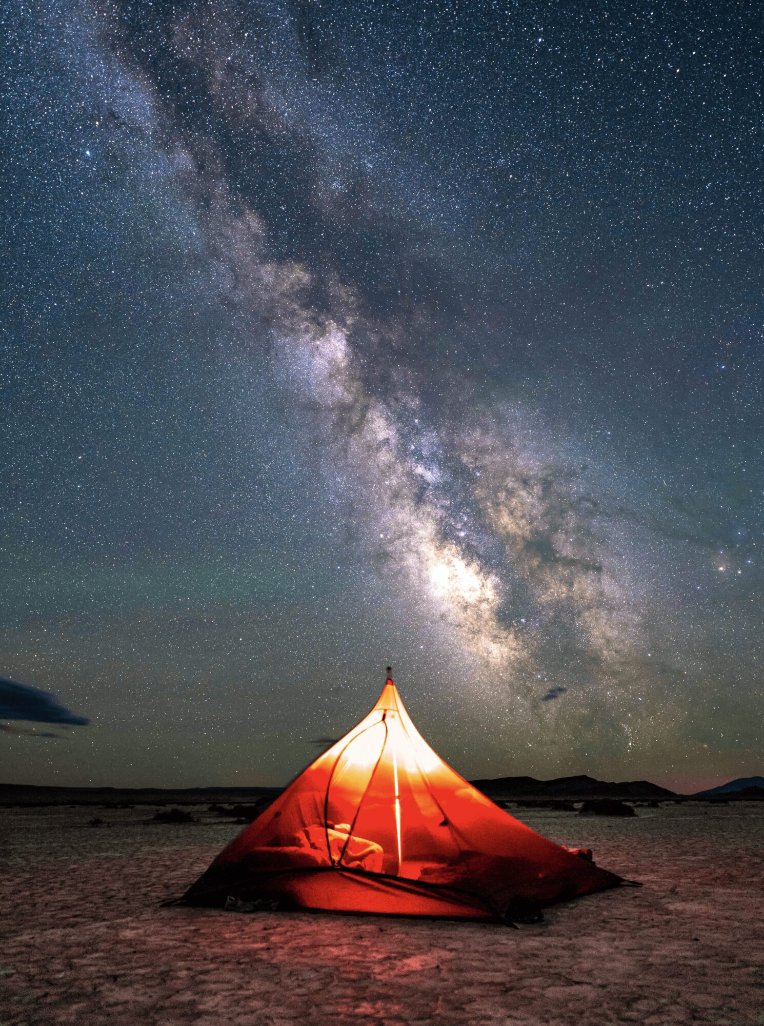 Tent on a beach under a starry night sky with the Milky Way galaxy visible above.