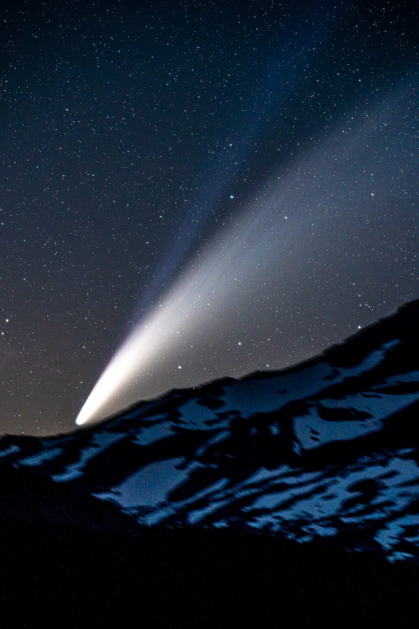 Night sky with stars and a bright comet or meteor over snow-covered mountains, illuminated by the celestial display.
