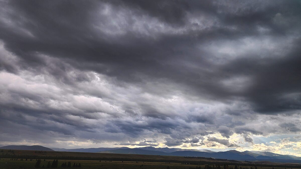 Dark, cloudy sky over a flat landscape with distant mountains, stormy weather, and heavy cloud cover.