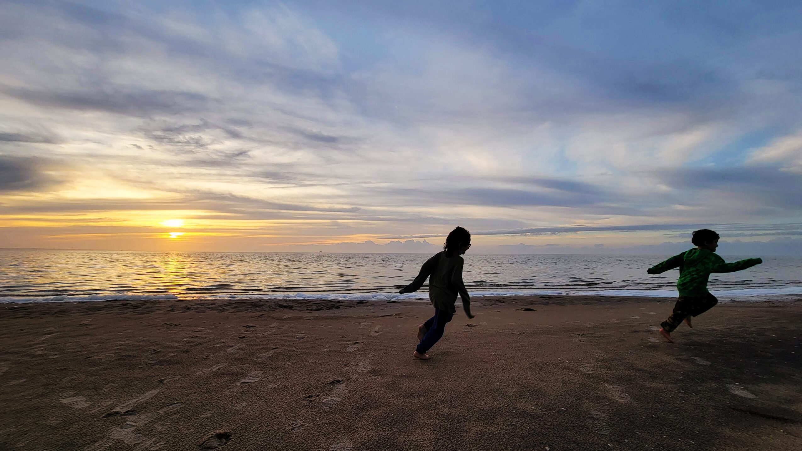 Two children playing on a beach during sunset, with the ocean and sky in the background.