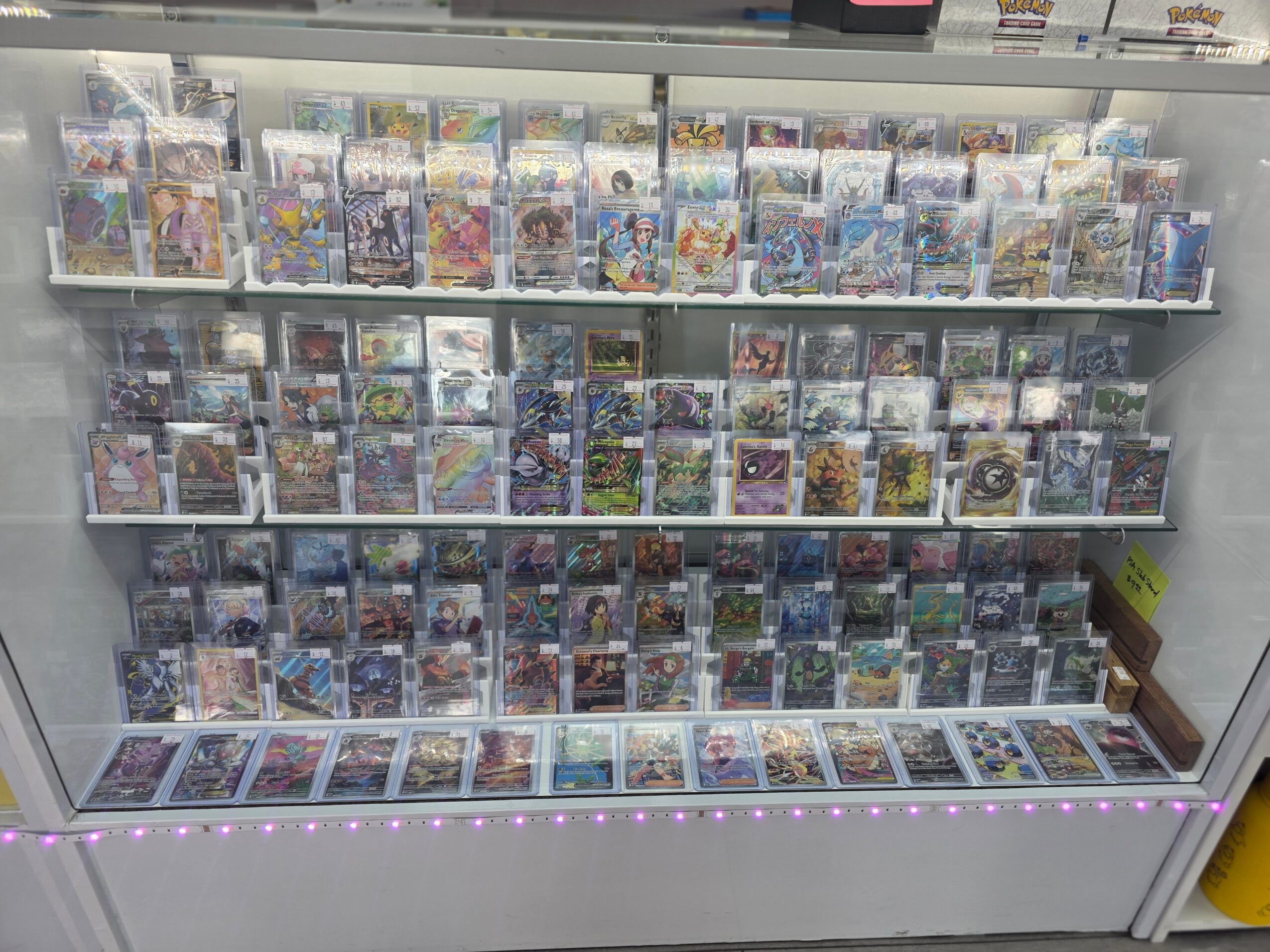 Display case filled with video game cases arranged on shelves, with a row of cases at the bottom inside the case.