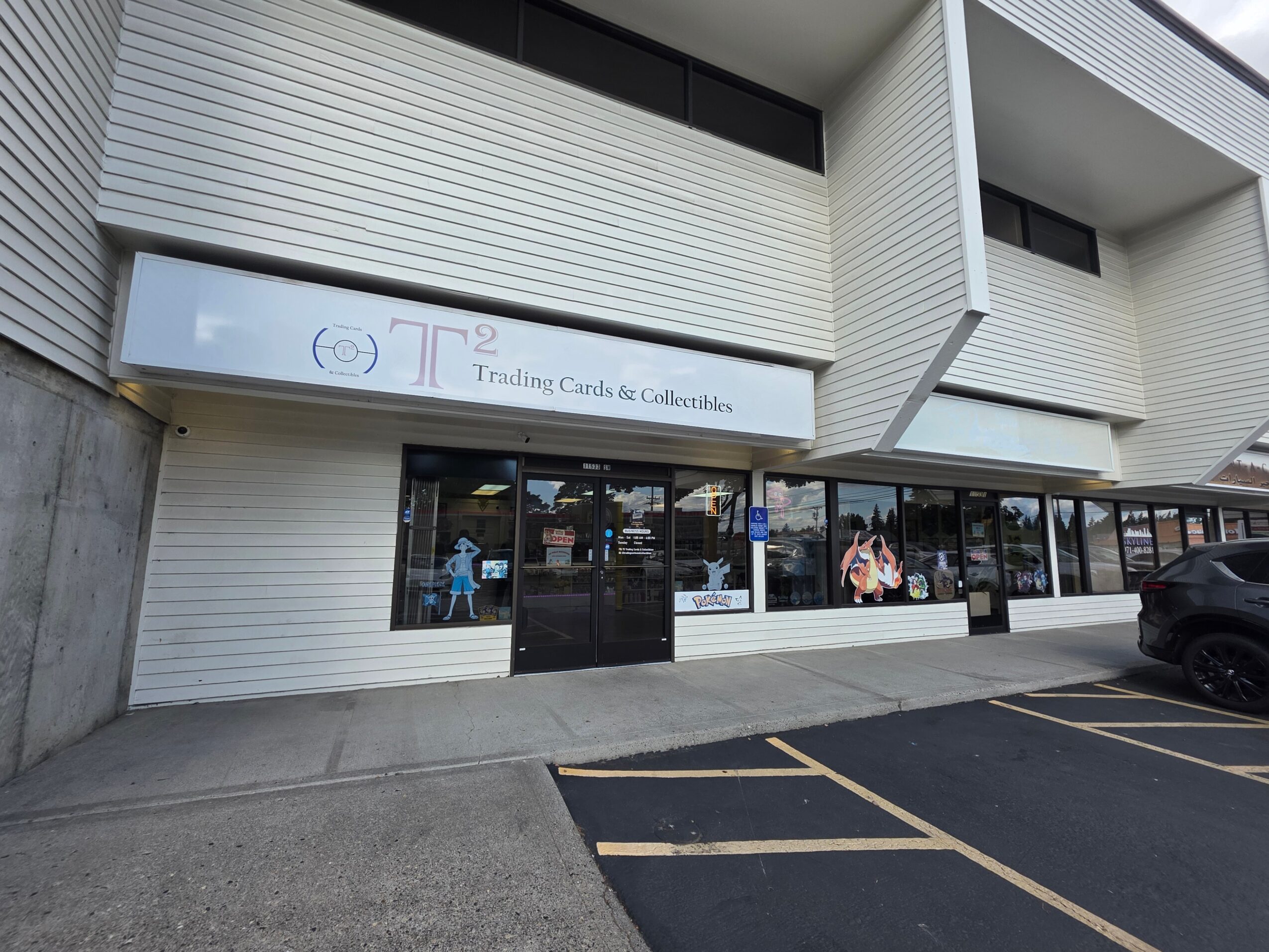 Storefront with large glass windows and a sign reading Trading Cards & Collectibles, parking lot in front, building exterior white with horizontal lines.