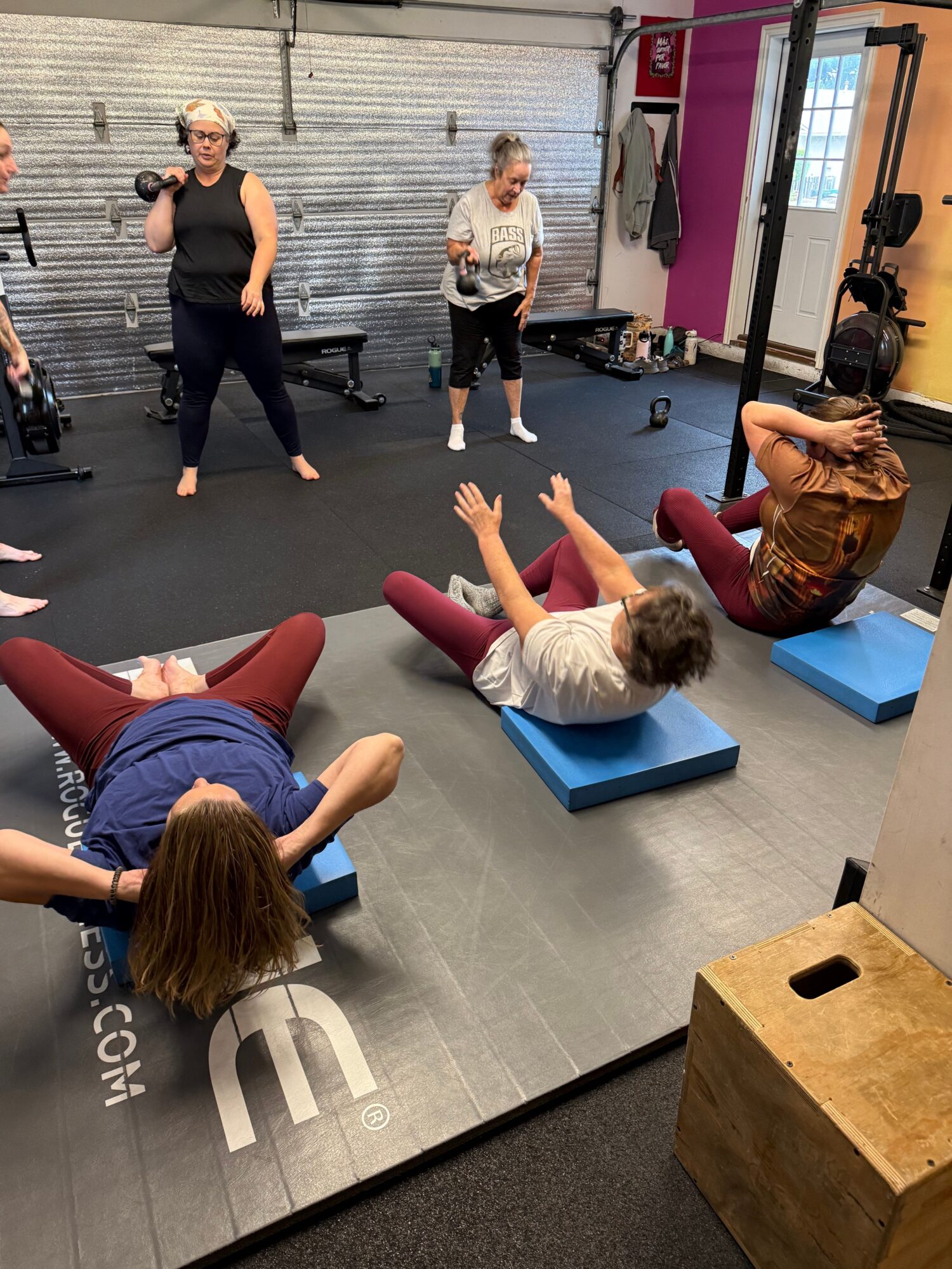 Three women and a girl in a gym, with mats and equipment, engaging in fitness activities.