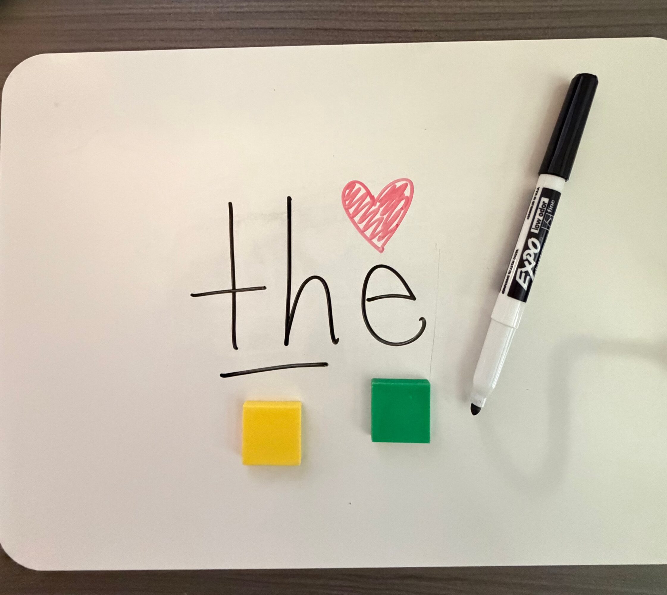 Whiteboard with the word 'the', a red heart, a yellow block, and a green block, with a black marker nearby.