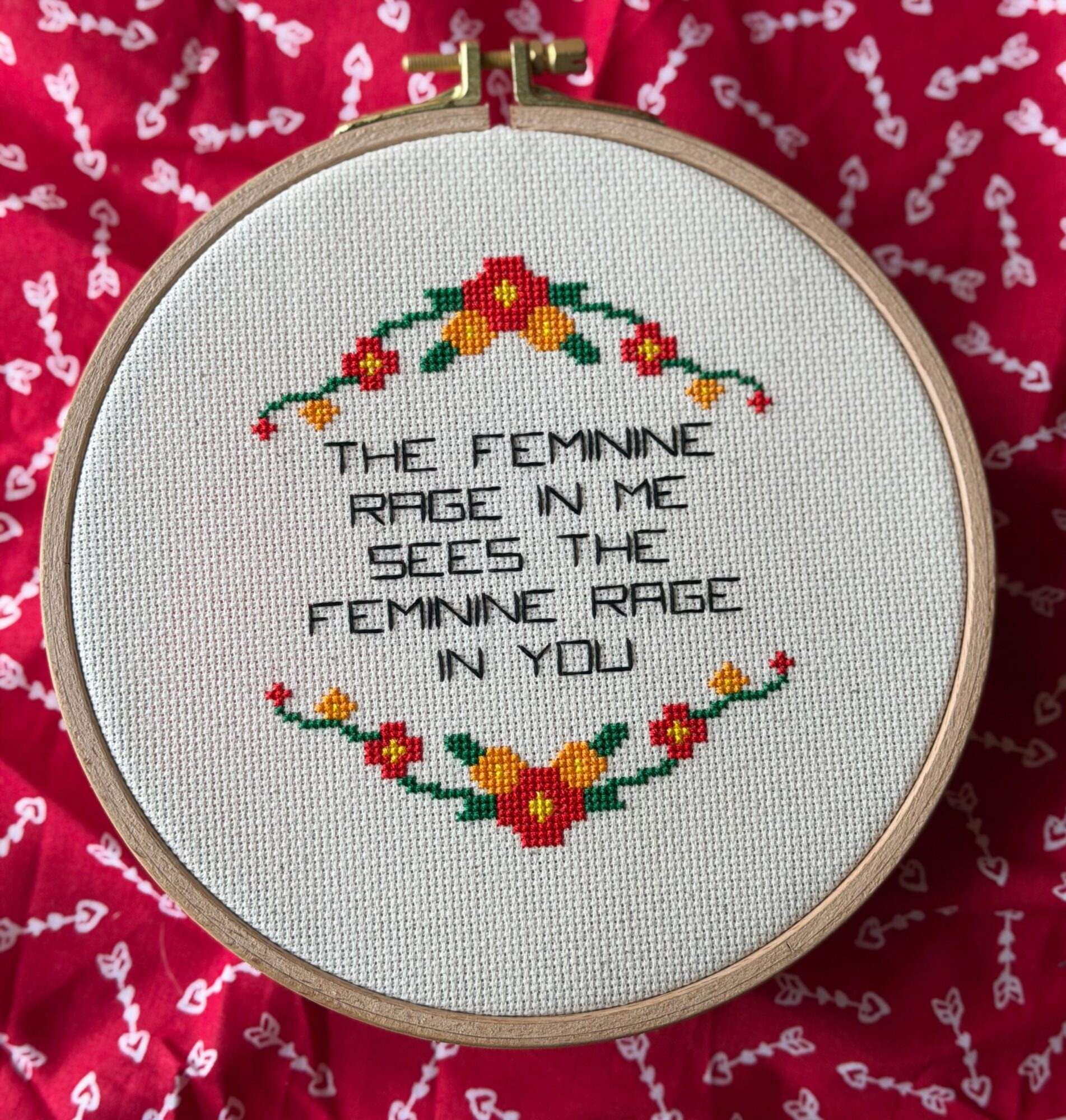 Cross-stitch embroidery with a floral design and the text, on a red fabric background. Word count: 20. Confidence: 0.9