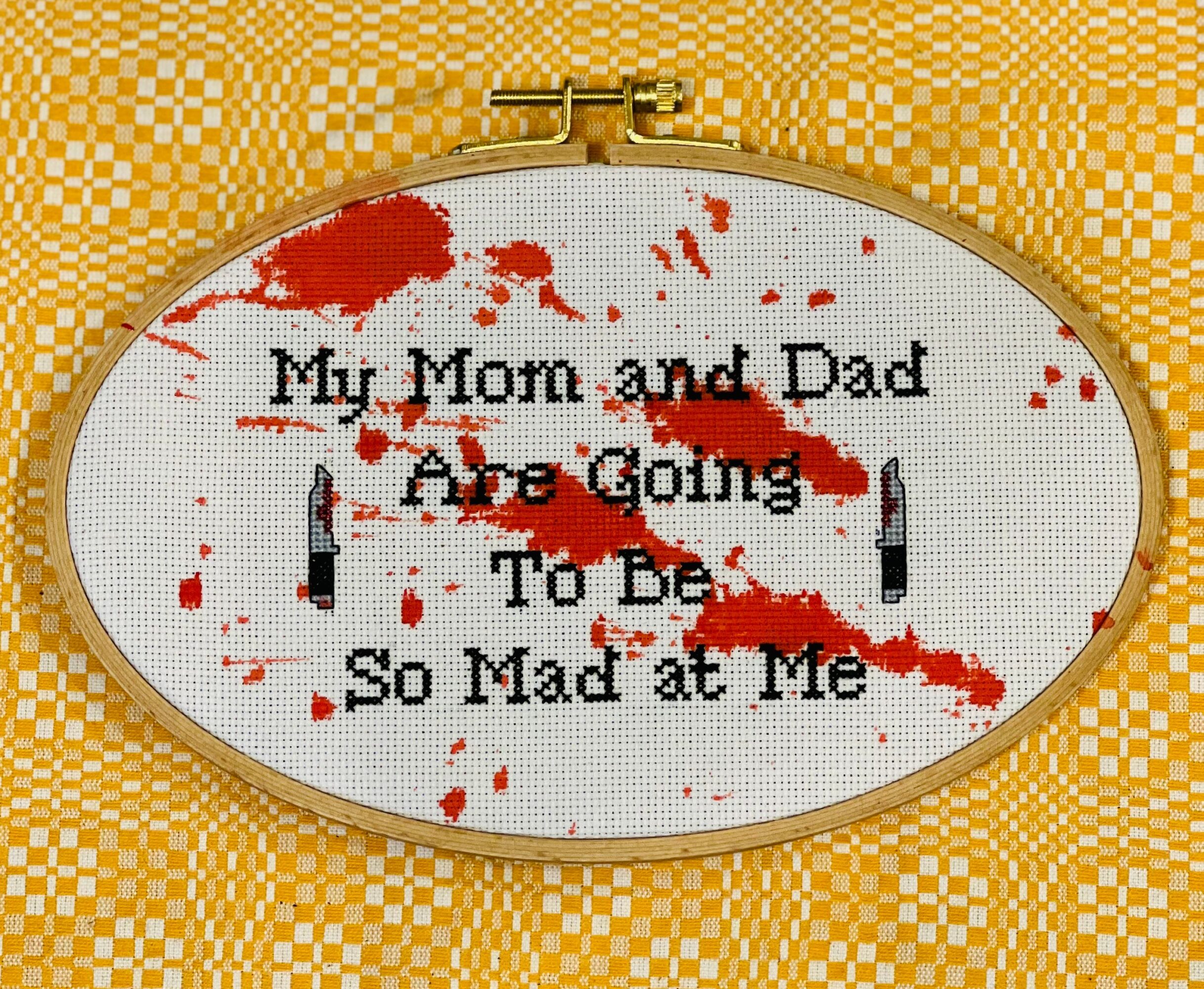 Embroidery hoop with text: 'My Mom and Dad Are Going To Be So Mad at Me' with red paint splatters, on yellow checkered fabric.