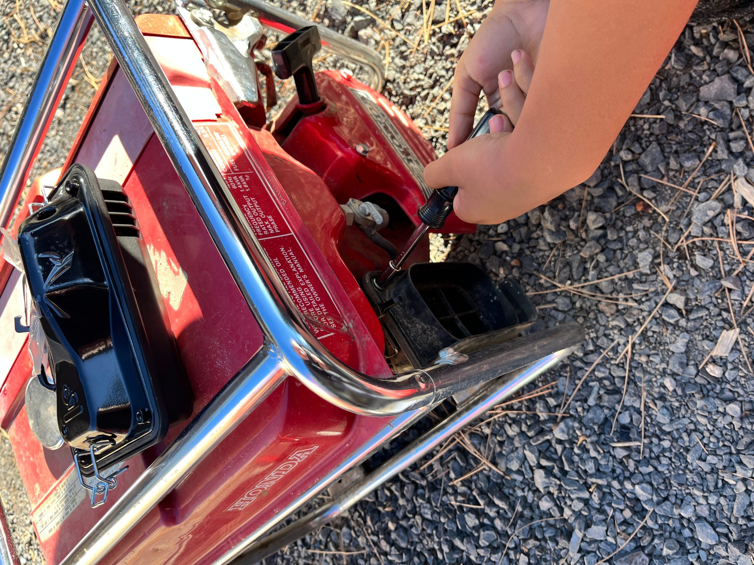 Child's hand adjusting a red control panel on a small vehicle or toy, with gravel ground nearby.