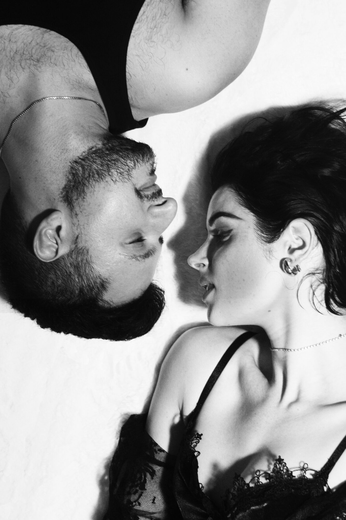 Two women lie face to face, eyes closed, with their heads close together on a white surface.