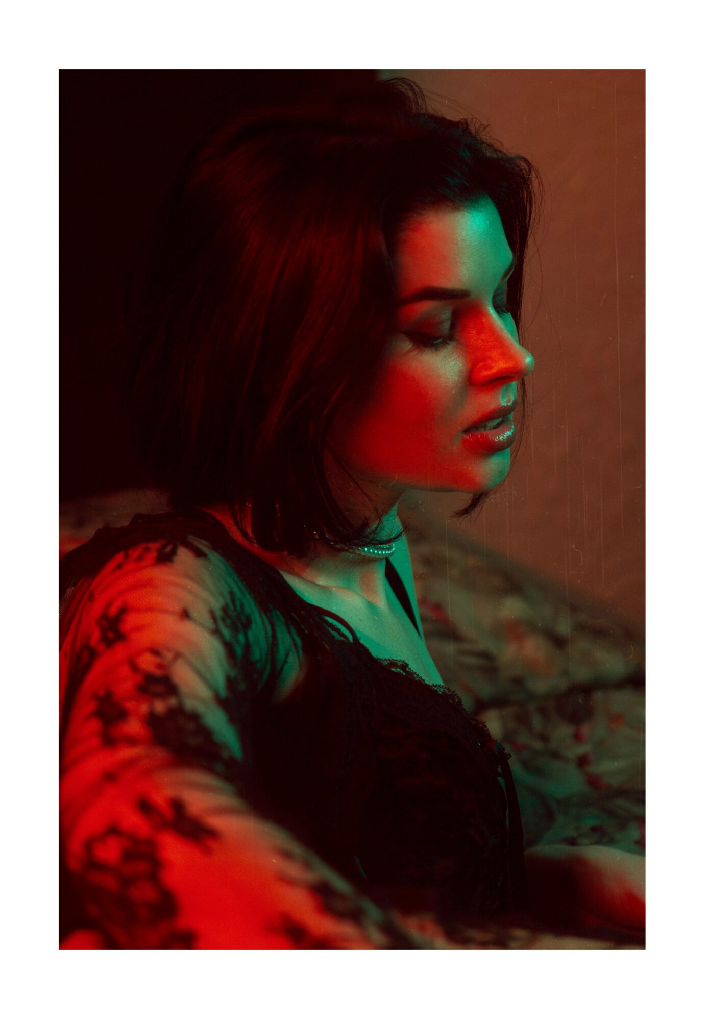 Side profile of a woman with short dark hair, illuminated by red and green lighting, with closed eyes and a contemplative expression.