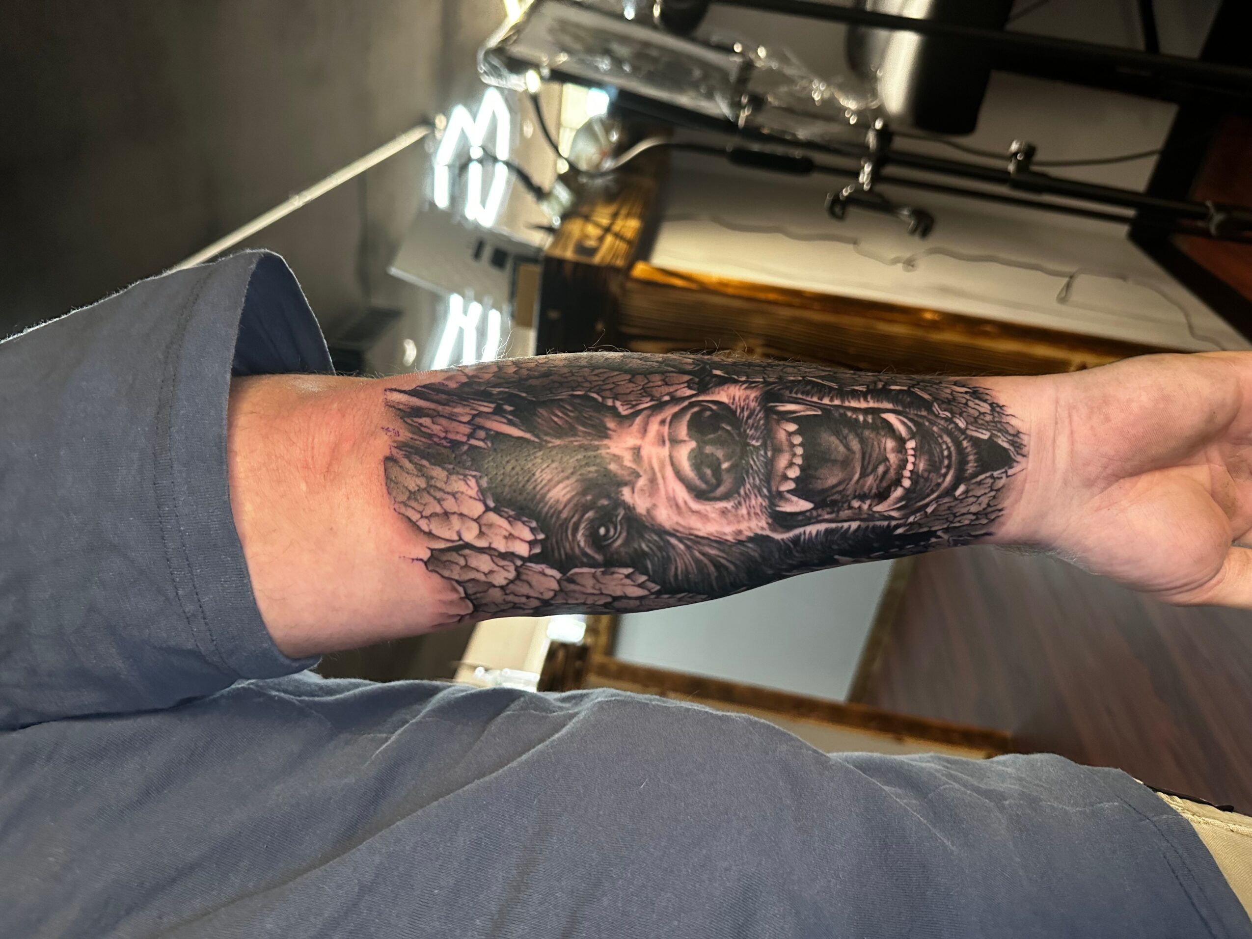 Forearm tattoo of a detailed face with an open mouth and surrounding intricate designs, visible on a person's arm.
