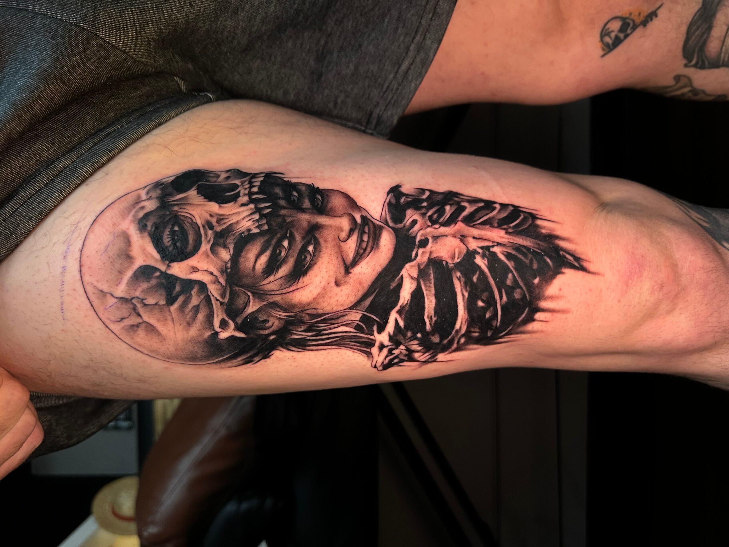Black and gray tattoo of a woman's face with skull elements on upper arm, detailed shading, realistic style.