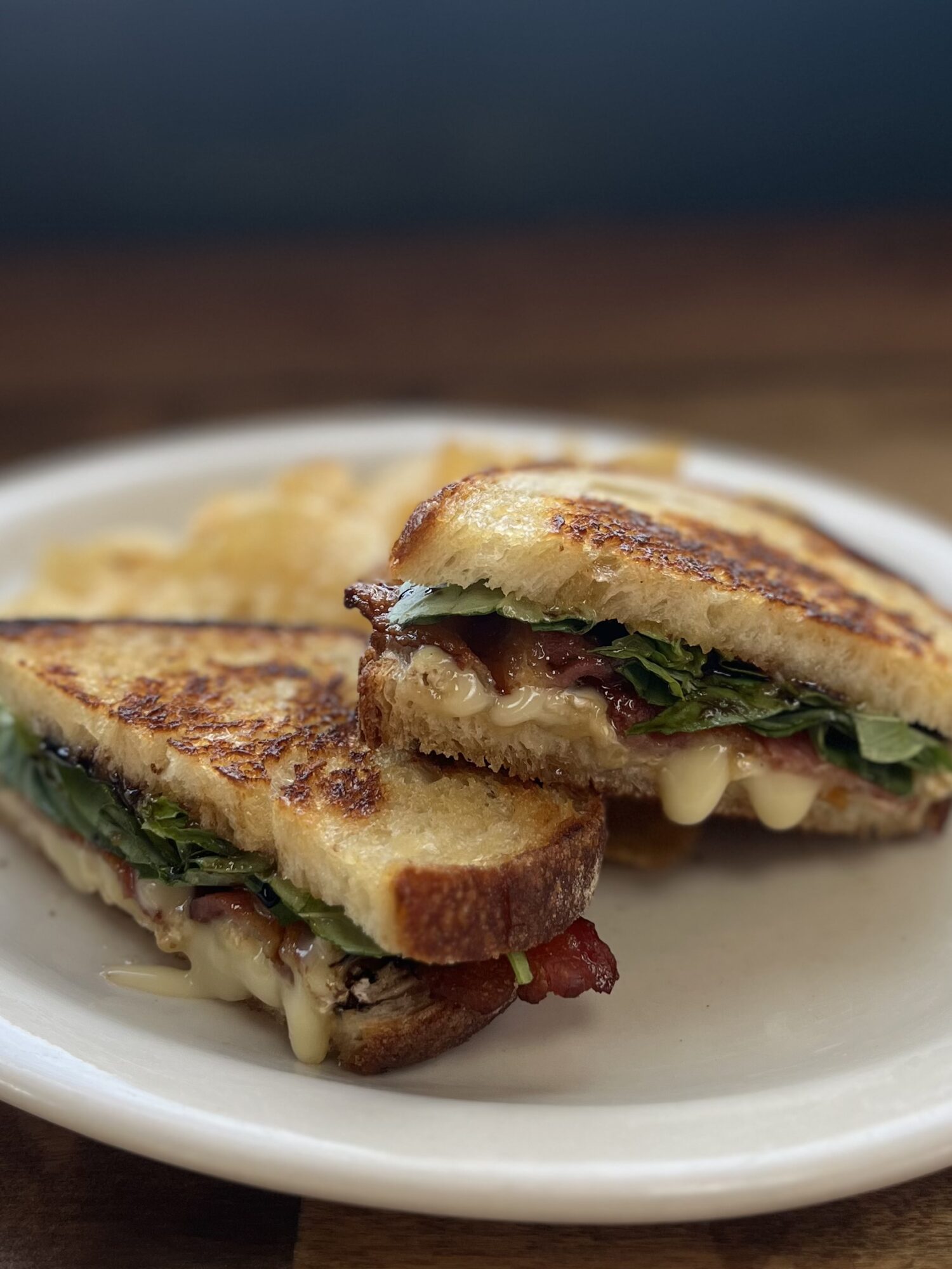 Two grilled sandwiches cut in half on a white plate, showing melted cheese, greens, and bacon inside.