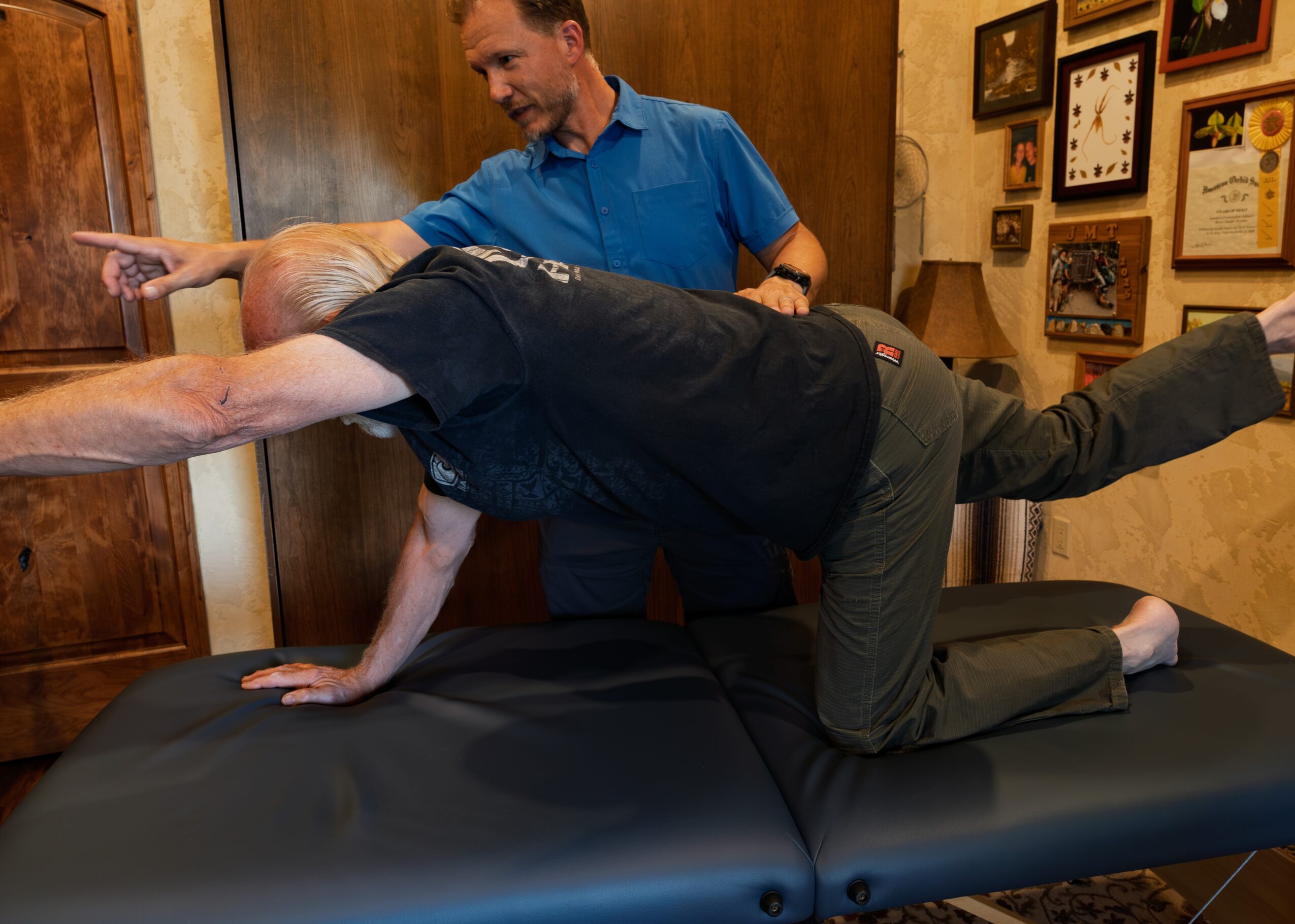 Person in black shirt on hands and knees on a table, with another person standing nearby pointing.