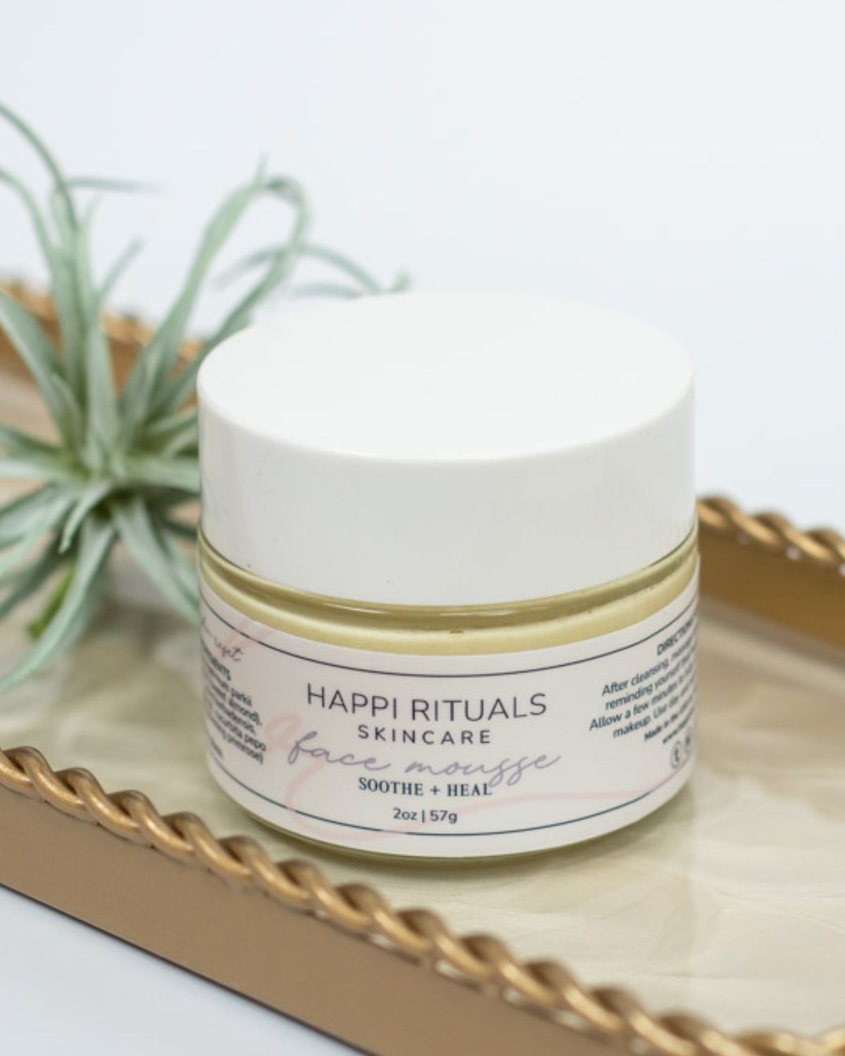 A white jar of skincare cream on a tray with a plant in the background.