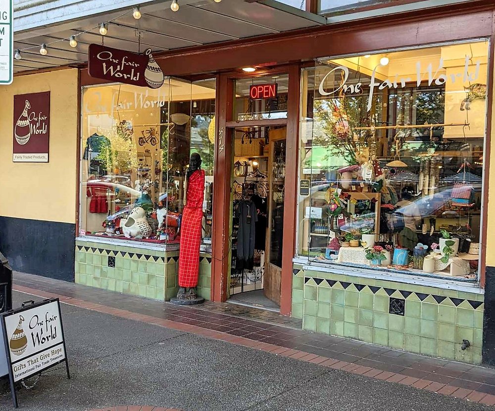 Storefront with large window display, open sign, and a mannequin in a red dress inside, with a sidewalk outside.