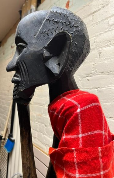Black carved sculpture of a human head with a red and white checkered cloth draped over the shoulder.