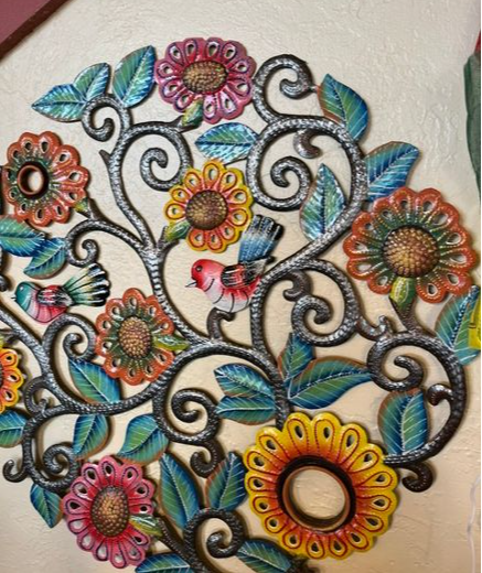 Decorative metal wall art with colorful flowers, leaves, and a small bird, mounted on a wall.
