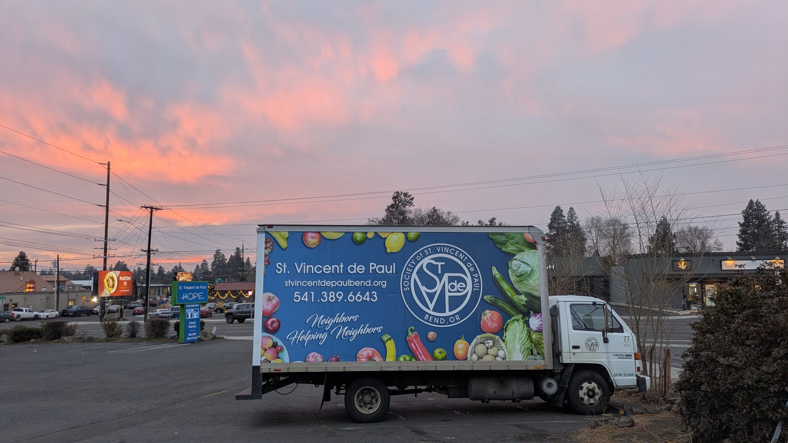 Truck with a colorful advertisement for St. Vincent de Paul, parked outdoors during sunset, with trees and power lines in background.