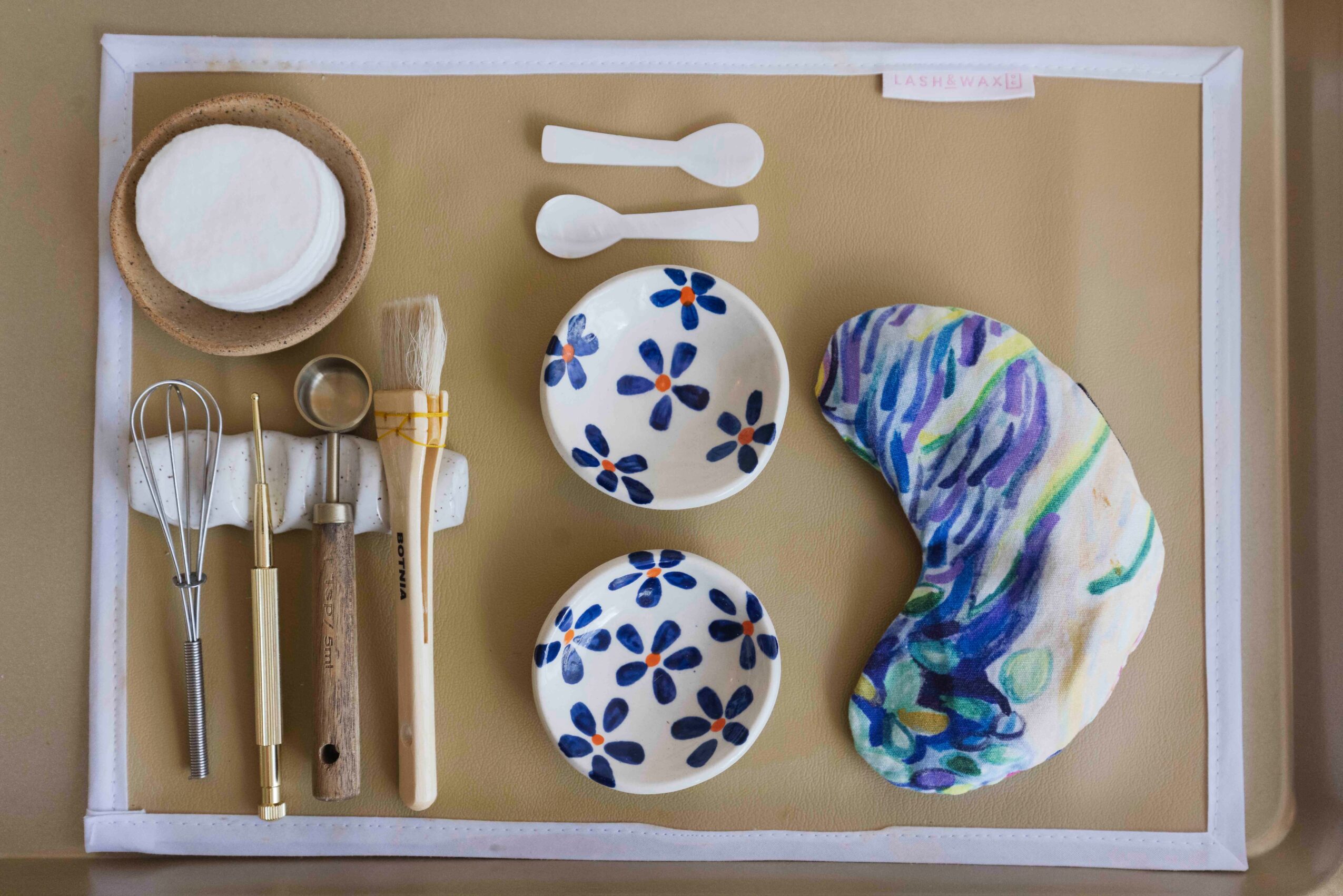 Assorted baking tools and ingredients on a tray, including spoons, bowls, a pastry brush, and a colorful dough piece.