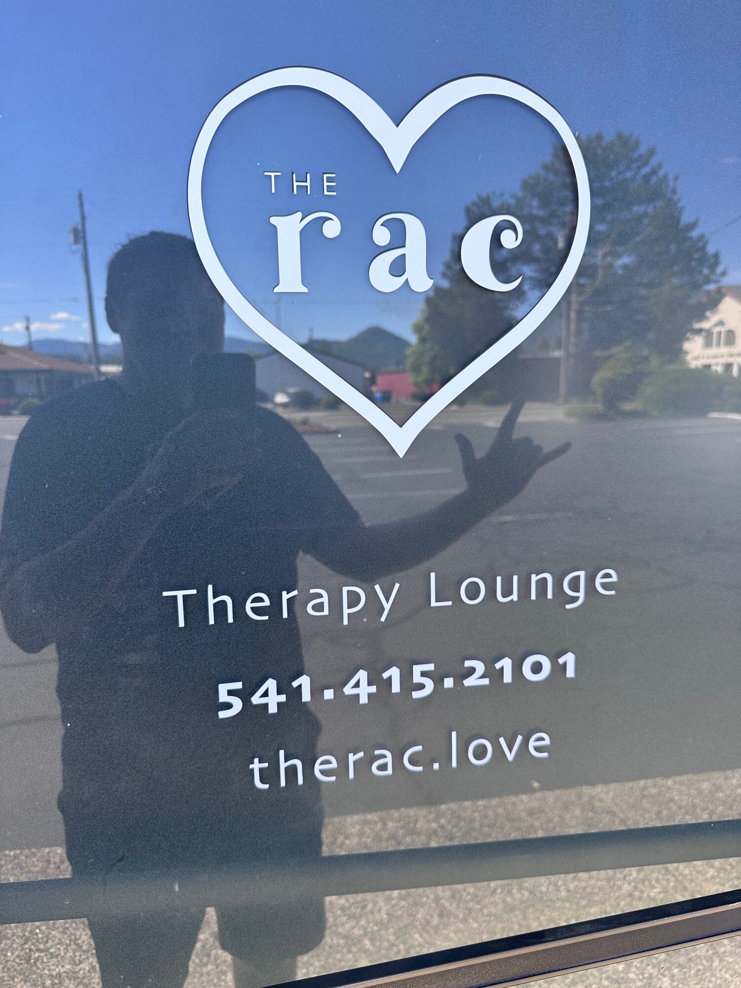 Reflection of a person taking a photo in a window with text about therapy lounge and contact information.