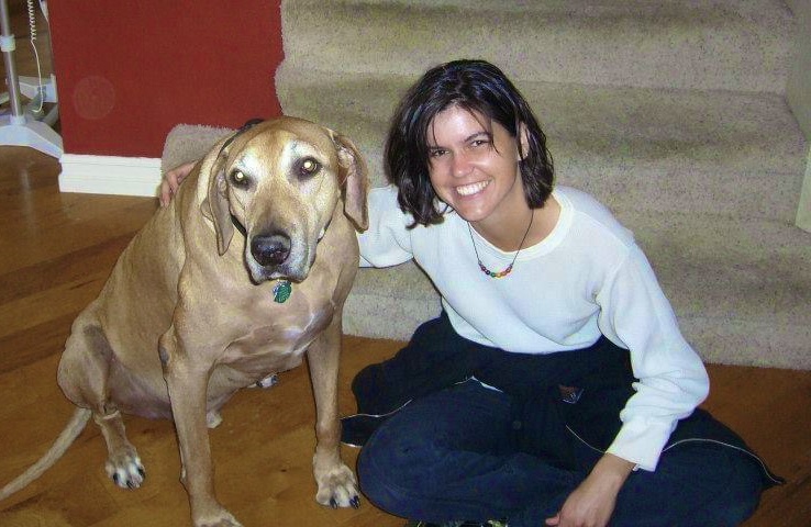 Woman sitting on stairs next to a large dog indoors, smiling at the camera.