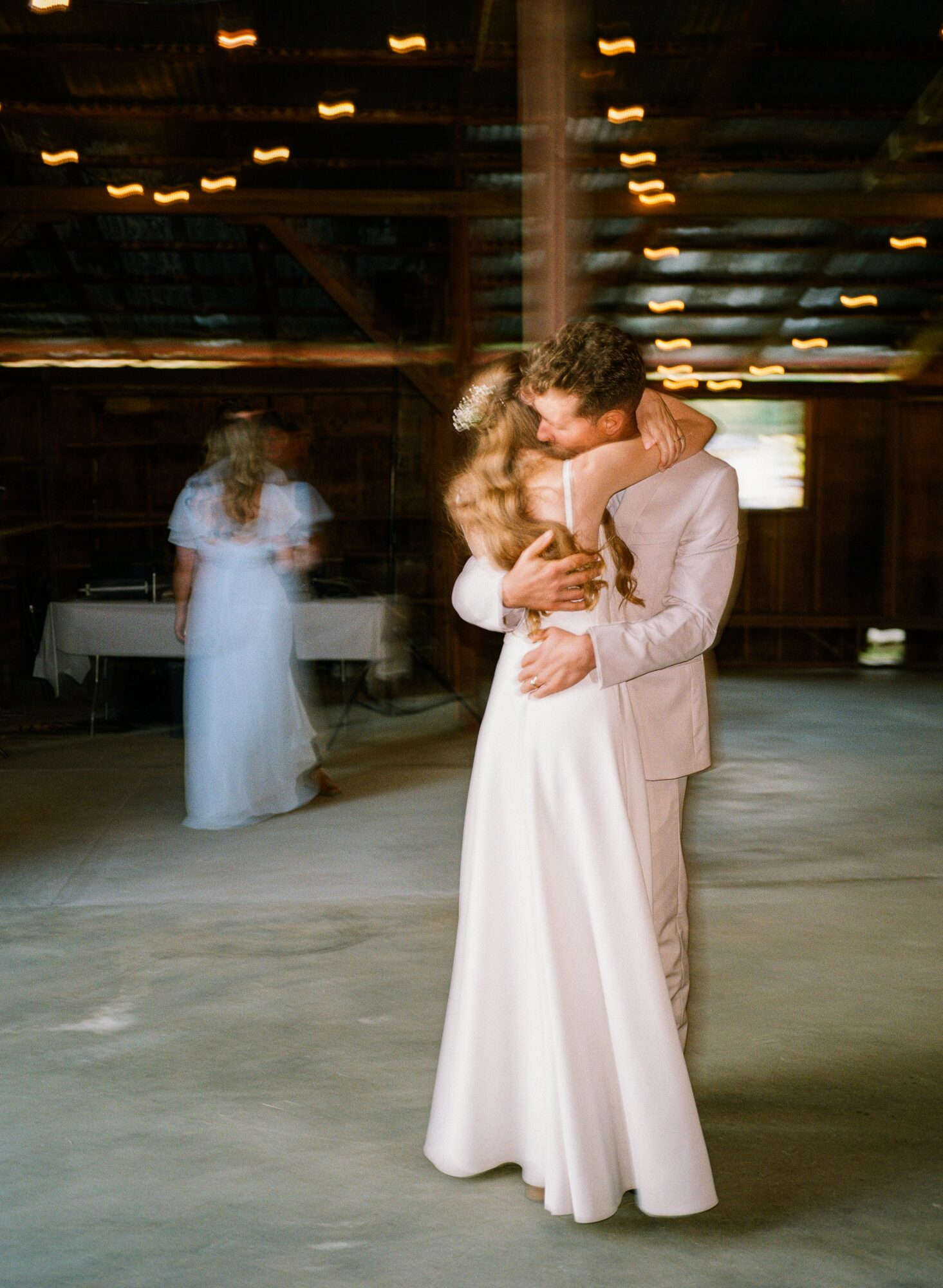 Couple dancing closely in a dimly lit venue, with a person in a white dress in the background.