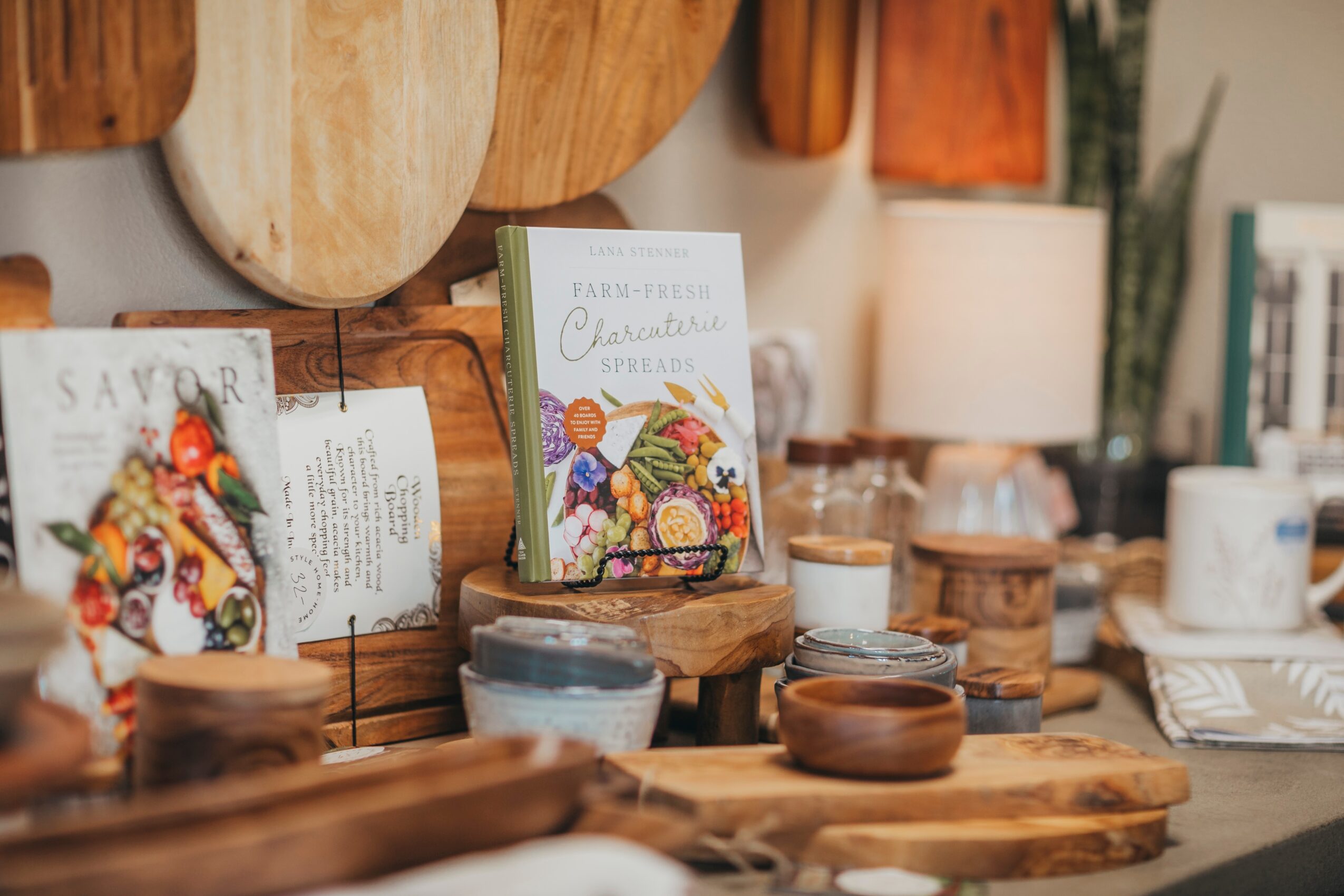 Display of cookbooks, bowls, and wooden serving boards on a table in a cozy setting.