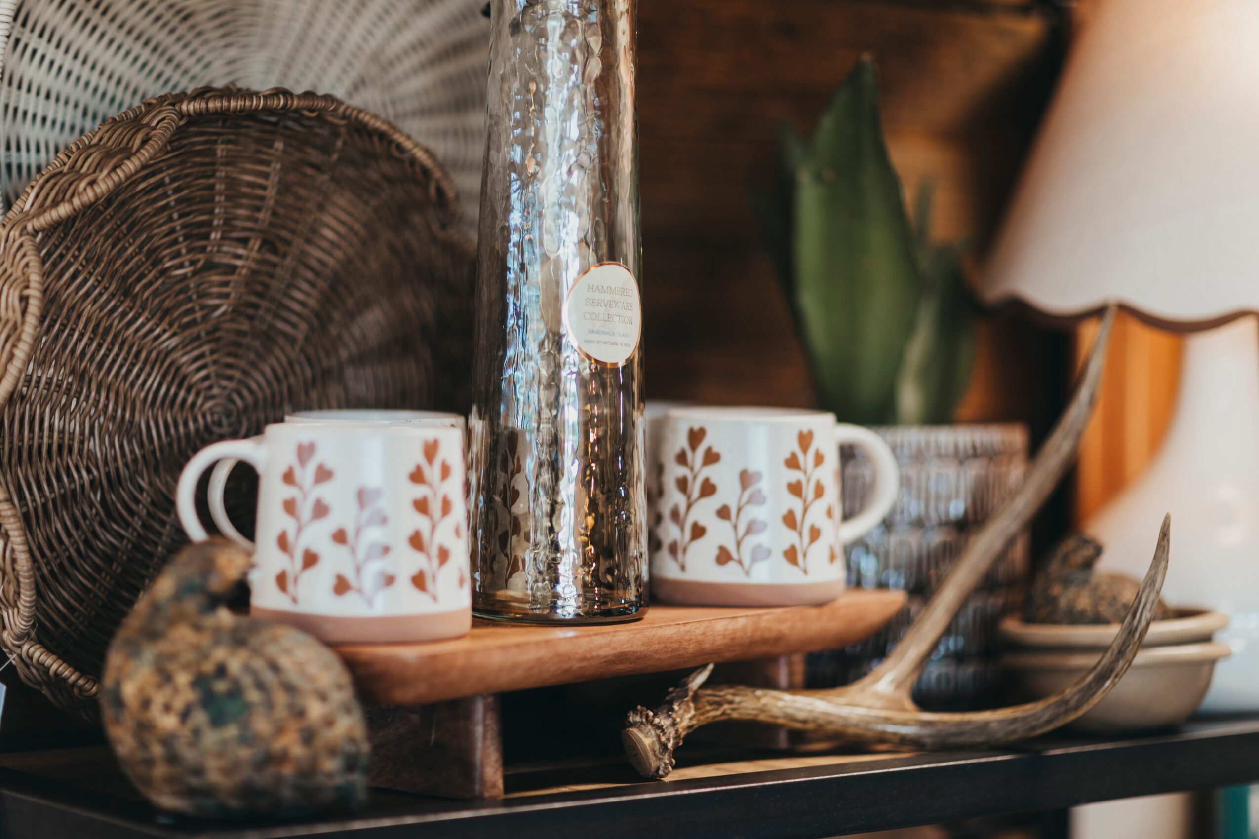 Two white mugs with leaf patterns, a tall silver container, and decorative objects on a black surface.