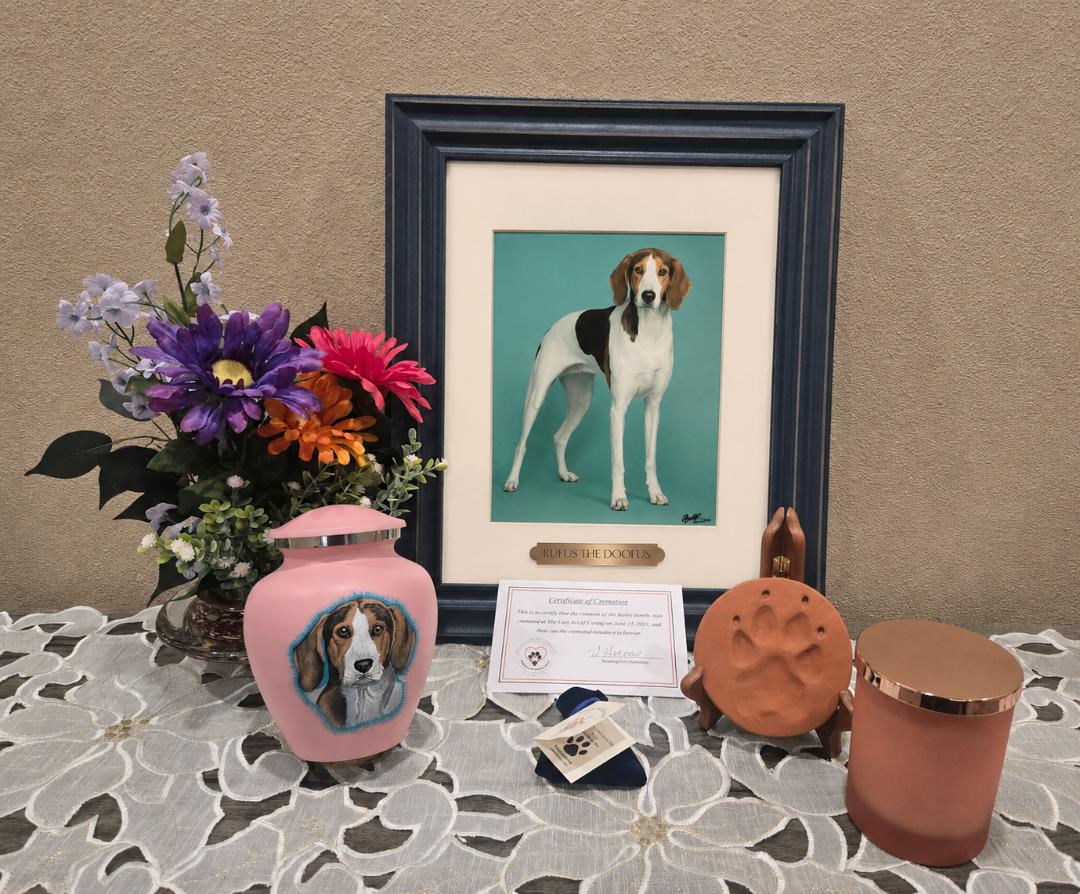 Display of dog-themed items including a framed photo, a painted vase, a plush toy, and decorative containers on a table.