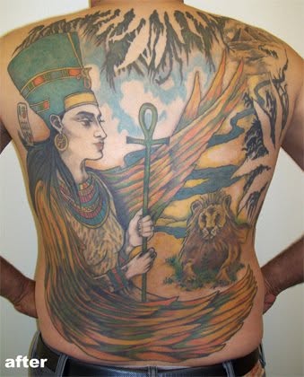 Colorful tattoo of an Egyptian queen holding an ankh, with a lion and landscape background, covering the person's back and side.