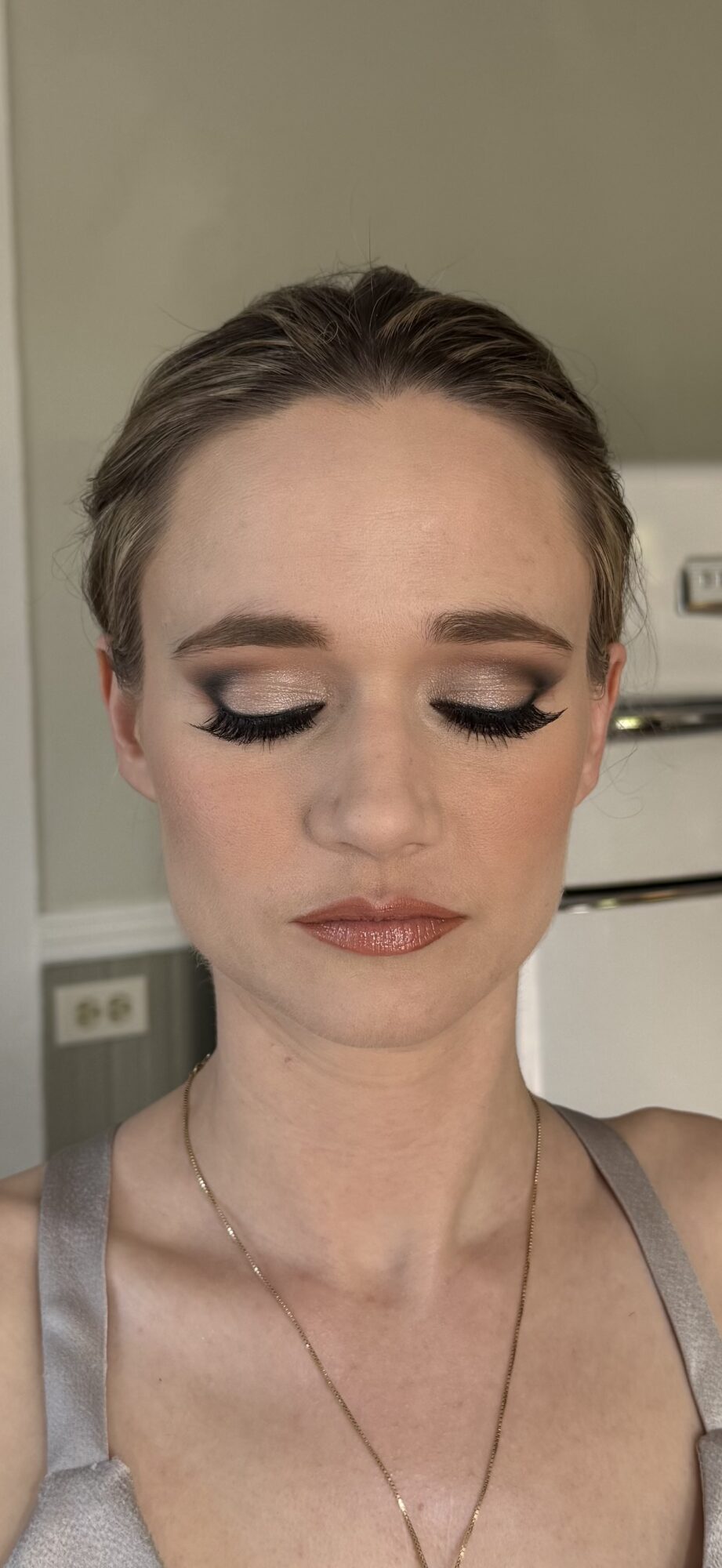 Woman with makeup, closed eyes, and a neutral background.
