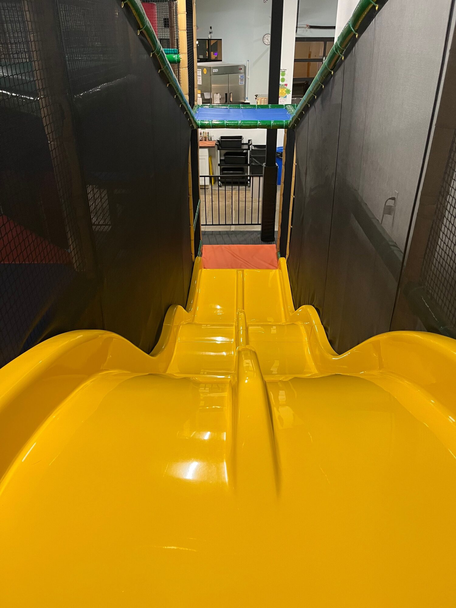 Yellow slide inside a play area with black and green surroundings, viewed from the side.