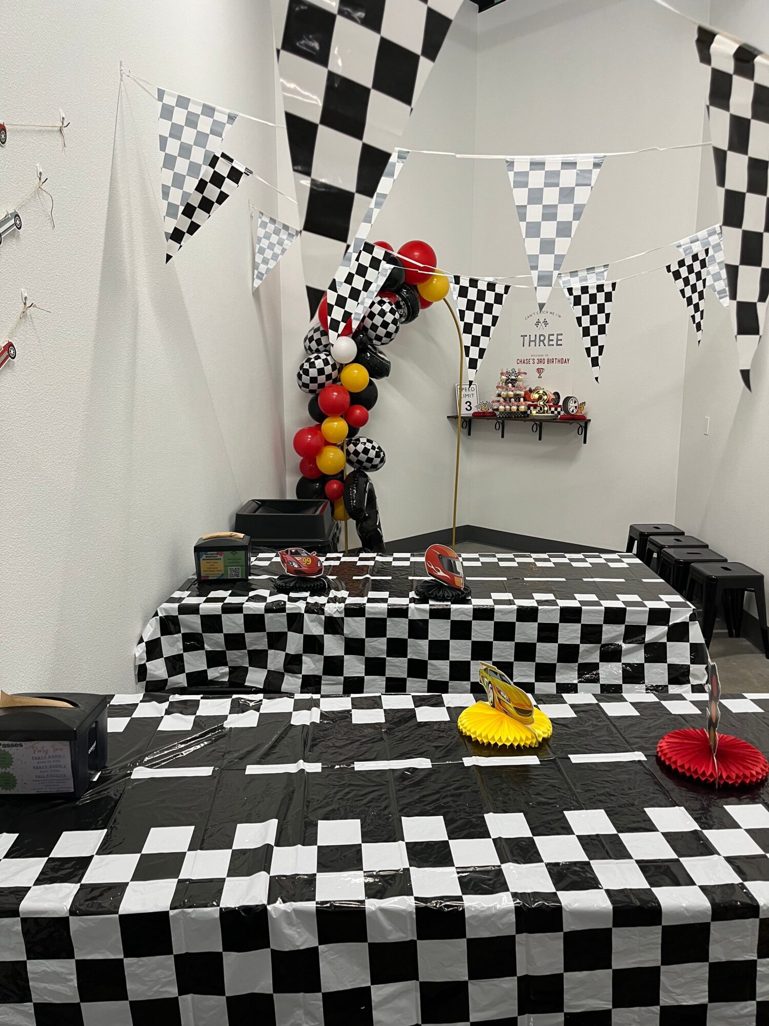 Party table with checkered tablecloth, balloons, and decorations in a room with checkered flags and black-and-white theme.