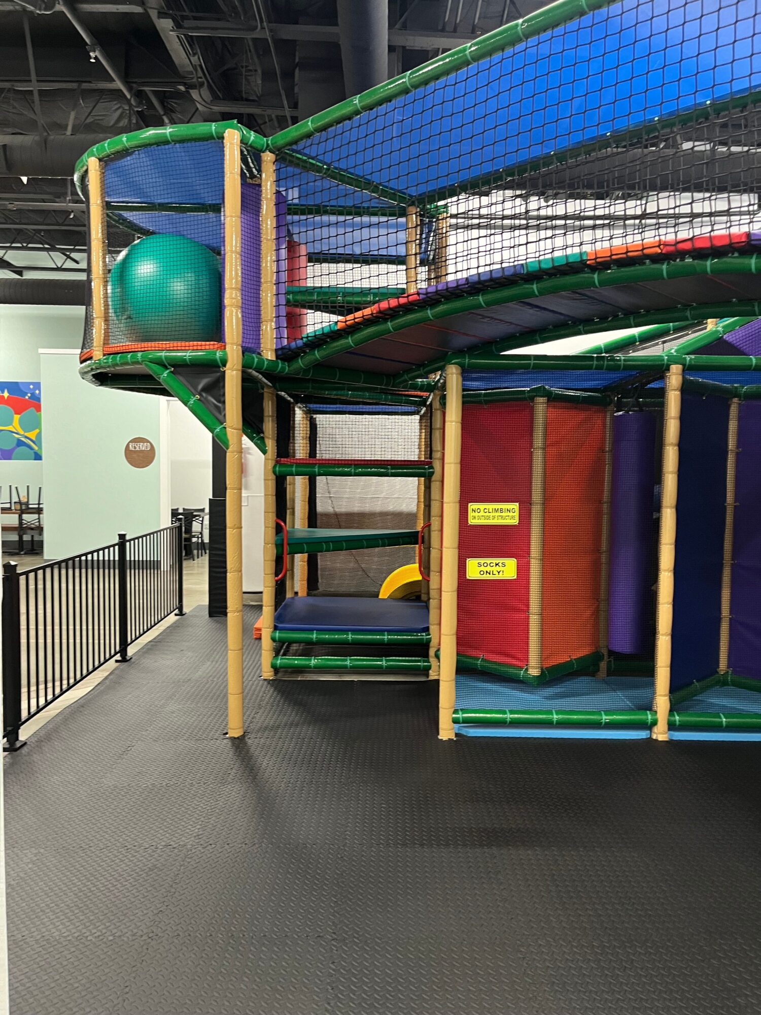 Indoor play area with colorful soft play structures, a ball, and a small gate, viewed from the side.