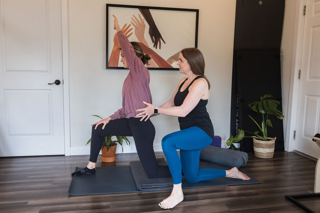 Two women practicing yoga in a room with a framed artwork, plants, and wooden flooring.