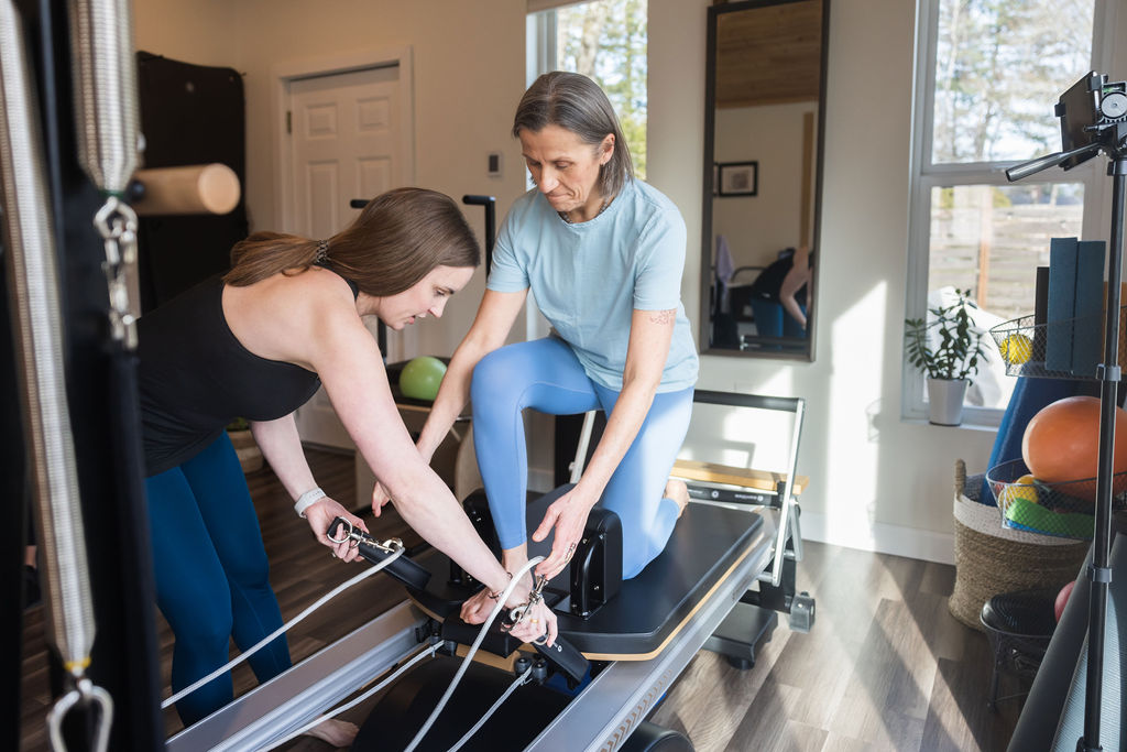 Two women assist a person on a treadmill in a bright room with large windows and a mirror.