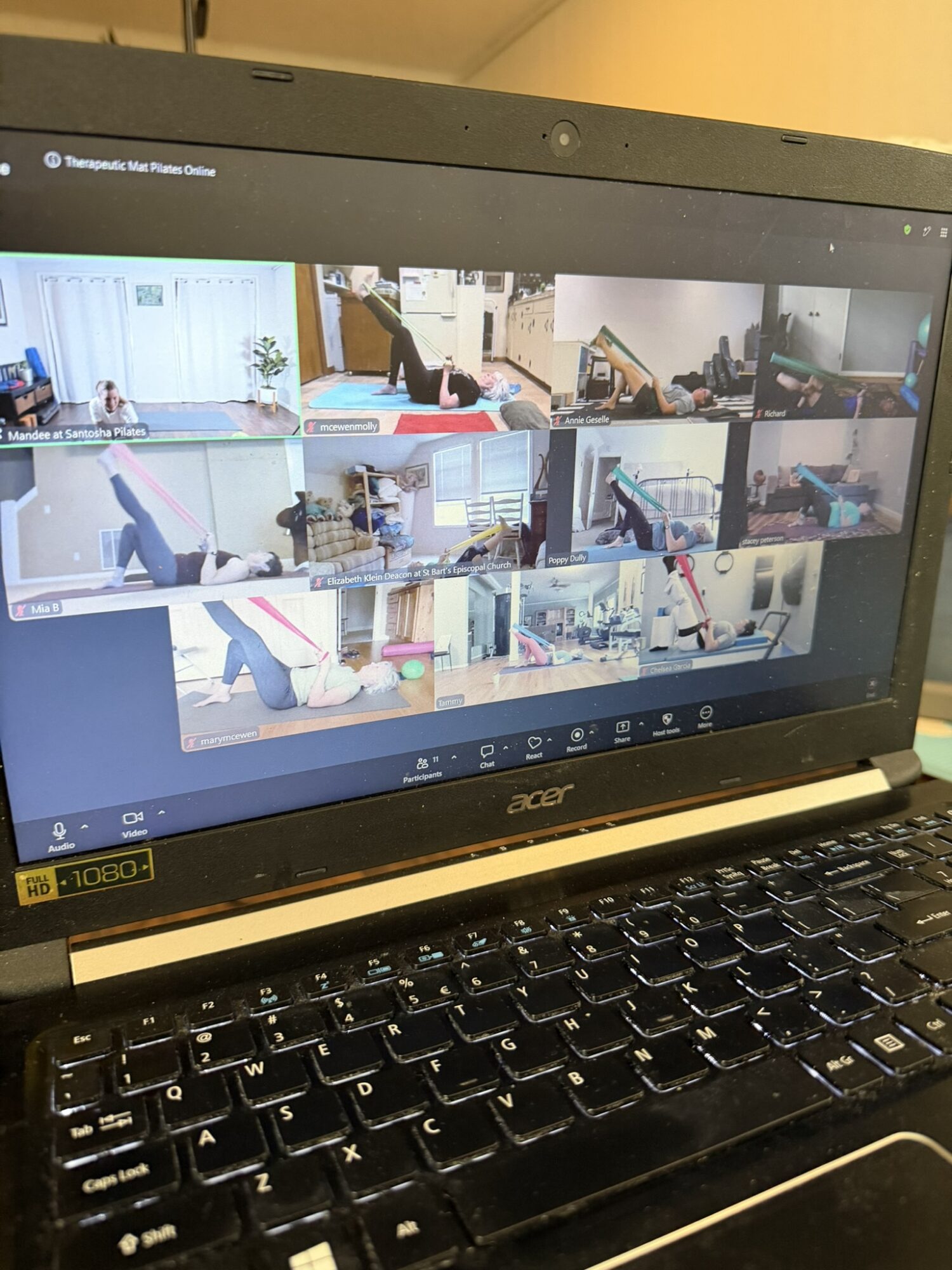 Laptop screen displaying multiple people practicing yoga or stretching exercises in various indoor settings.
